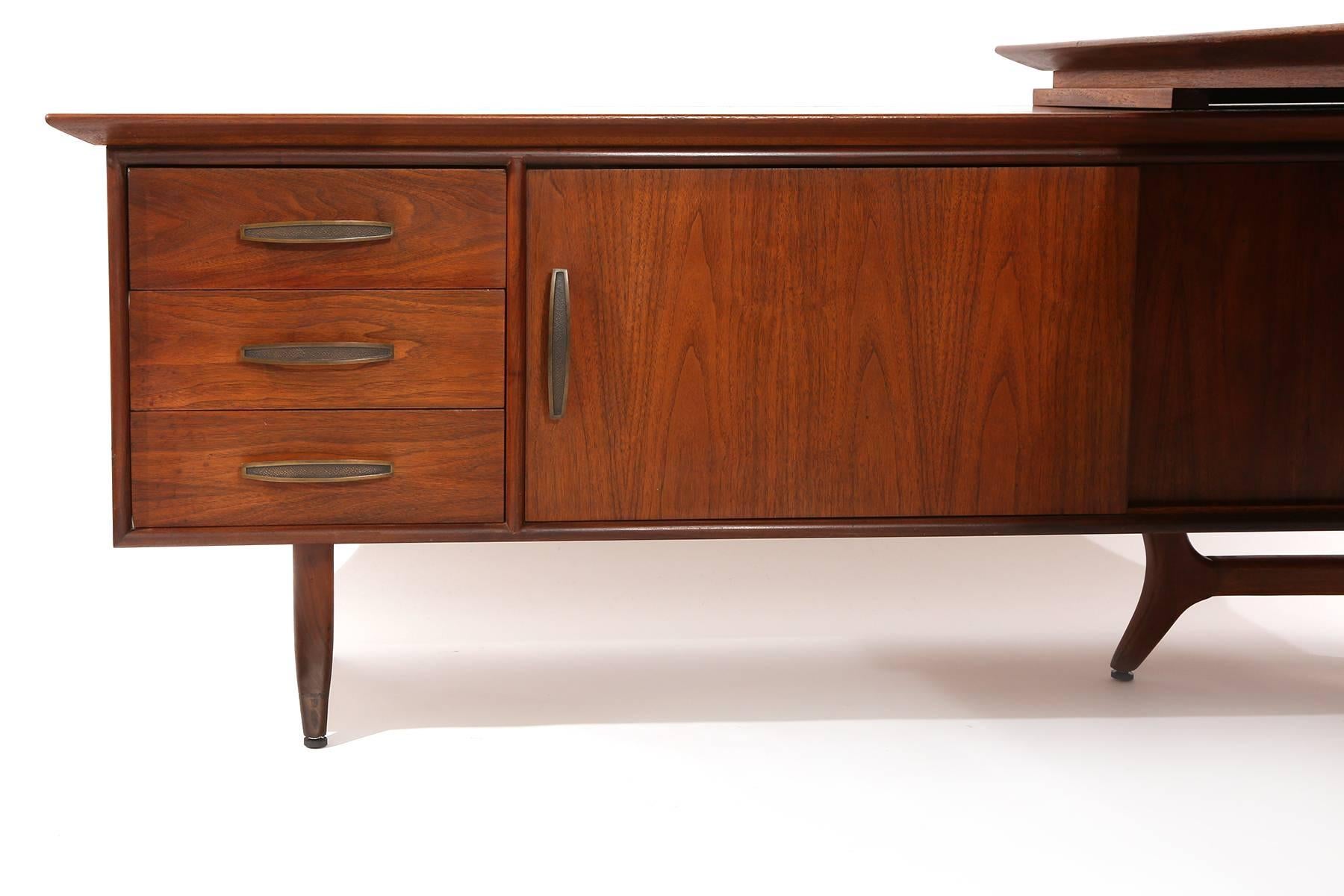 Desk and credenza by Modeline circa late 1950s. This example has pebbled brass handles solid walnut legs and banding and fantastic graining to the tops and sides.