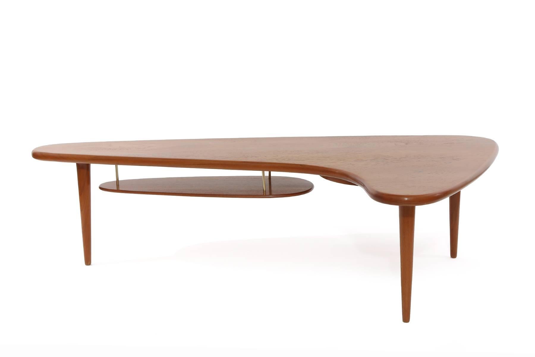 Free-form coffee table from Denmark, circa late 1950s. This example has a solid teak top and suspended solid teak second tier. It has a pull out black laminate circular section and brass accents. It has been newly and impeccably refinished.