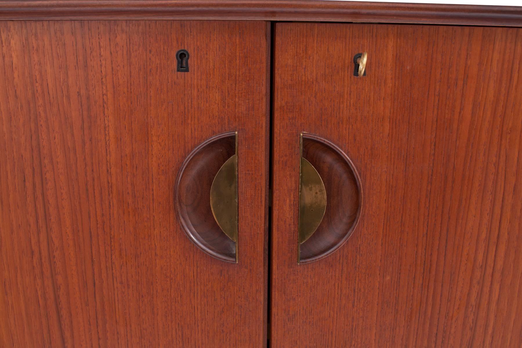 Stunning teak and brass sideboard from Denmark, circa mid-1950s. This all original example has a beautifully broken in solid teak frame, with inset patinated brass drawer pulls. It has five drawers and two doors that open to reveal plenty of