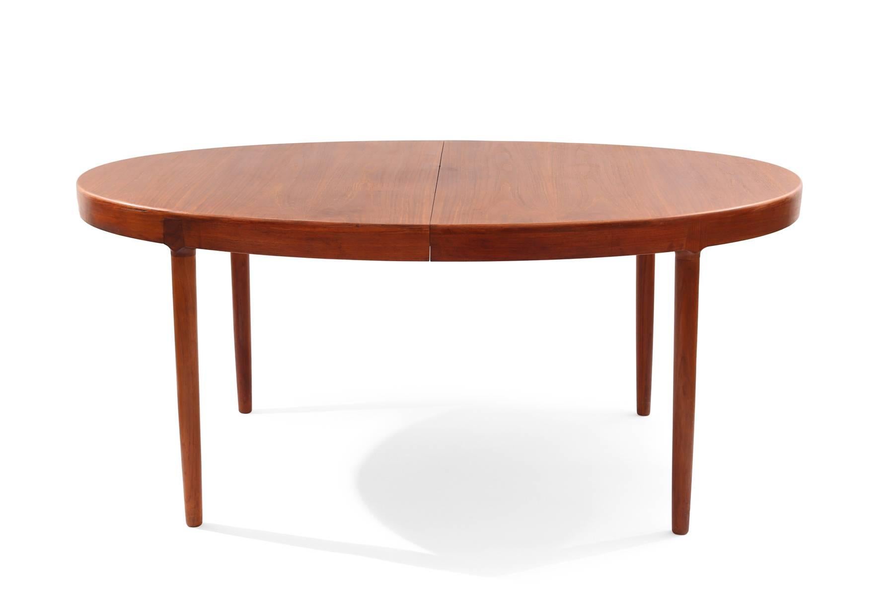 Ib Kofod-Larsen teak dining table, circa late 1950s. This all original example has inset solid teak legs, solid teak banding and beautifully grained teak top. Comes with two leaves. Each leaf measures 20