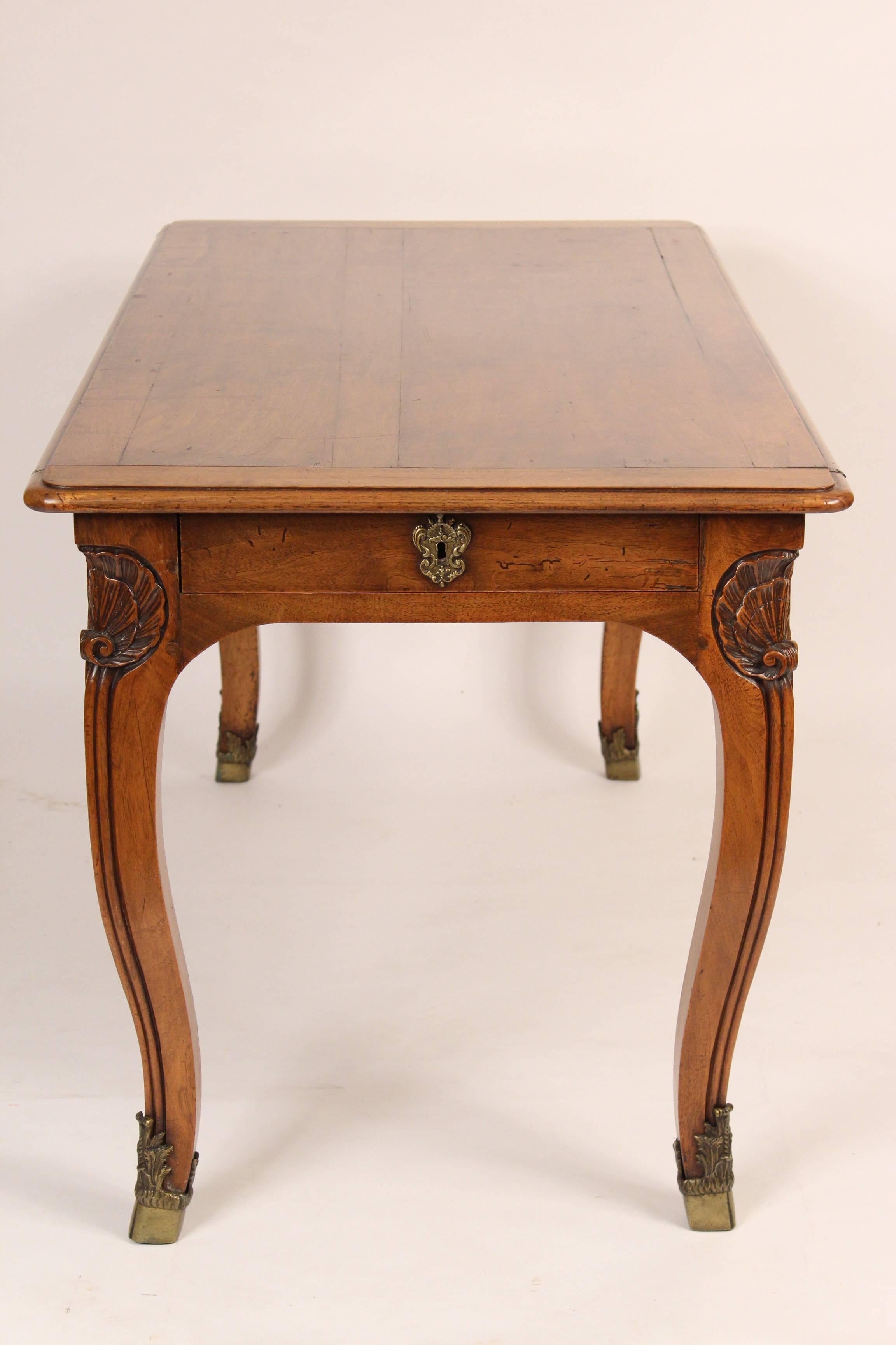 Louis XV Provincial style walnut writing table, circa 1890. This writing table features, shell carving on apron and legs, finely cast and chased bronze hoof form sabots. The drawers are on either end of the writing table. The distance from the
