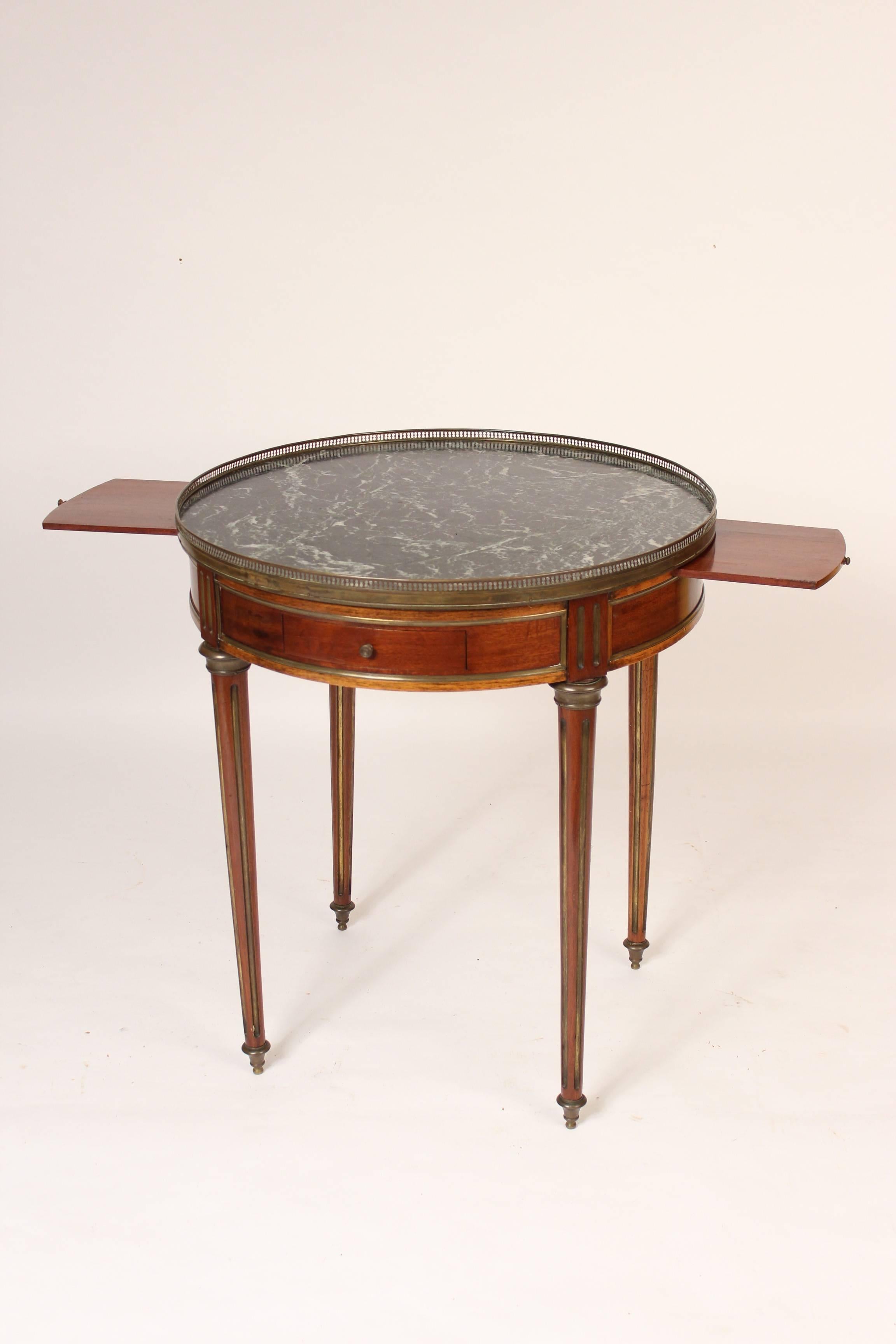 Louis XVI style mahogany bouillotte table with marble top, circa 1900. Features on this table include, fine quality mahogany panels on the frieze, brass inlaid legs, brass moldings on the frieze and reticulated brass gallery surrounding the marble