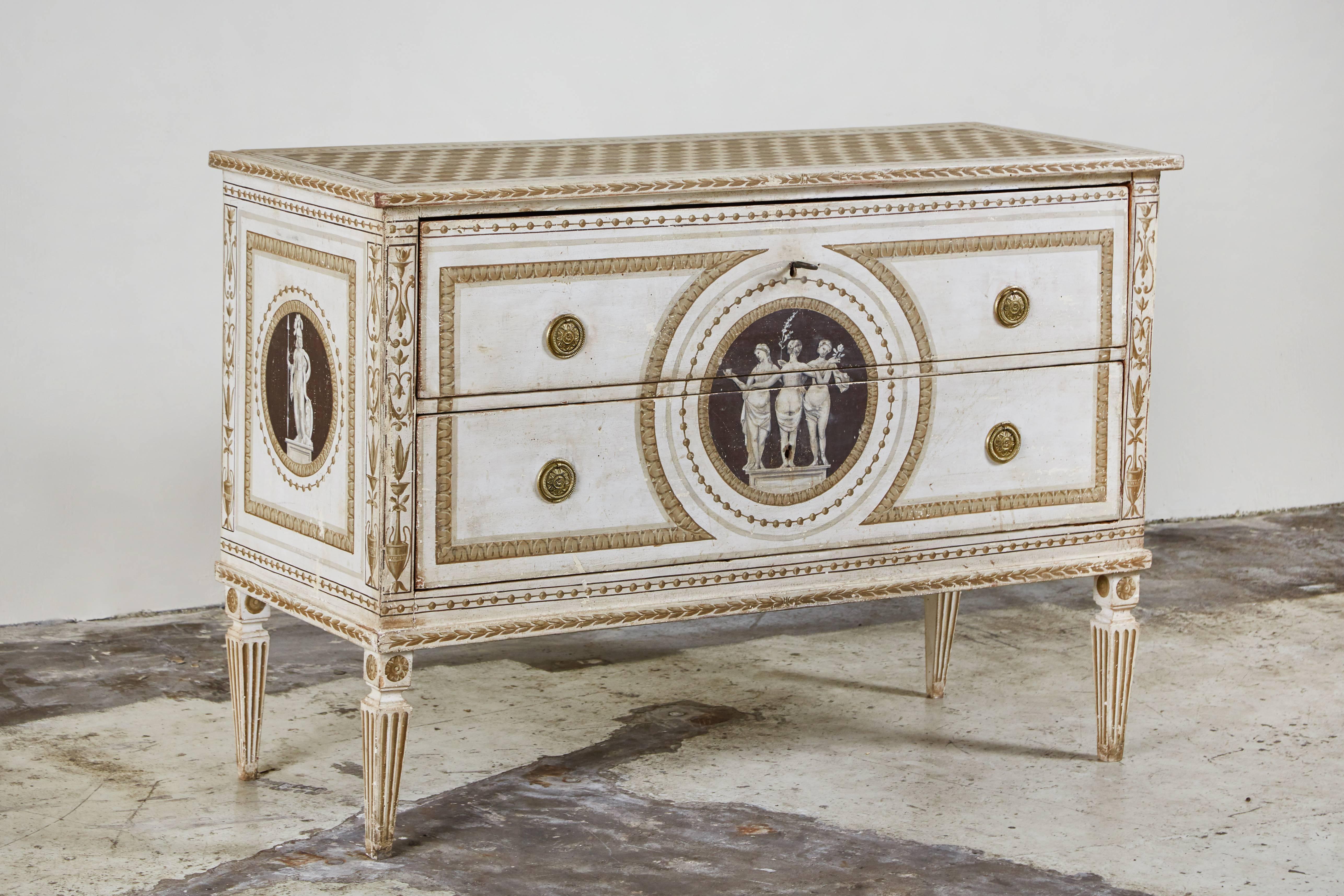 Elegant, circa 1870, two-drawer commode on tapered, fluted legs with striking, hand painting that dates to the 1920s. Embellishments include a stunning, central medallion depicting the Three Graces of Greek mythology and a faux-tiled top.