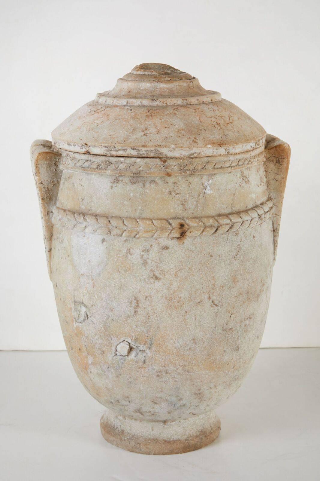 Elegant, 5th century Roman, marble urn featuring two relief bands of laurel leaves, faux, bifurcated, triangular armtitures and a gradated, carved lid. Wonderful patina.