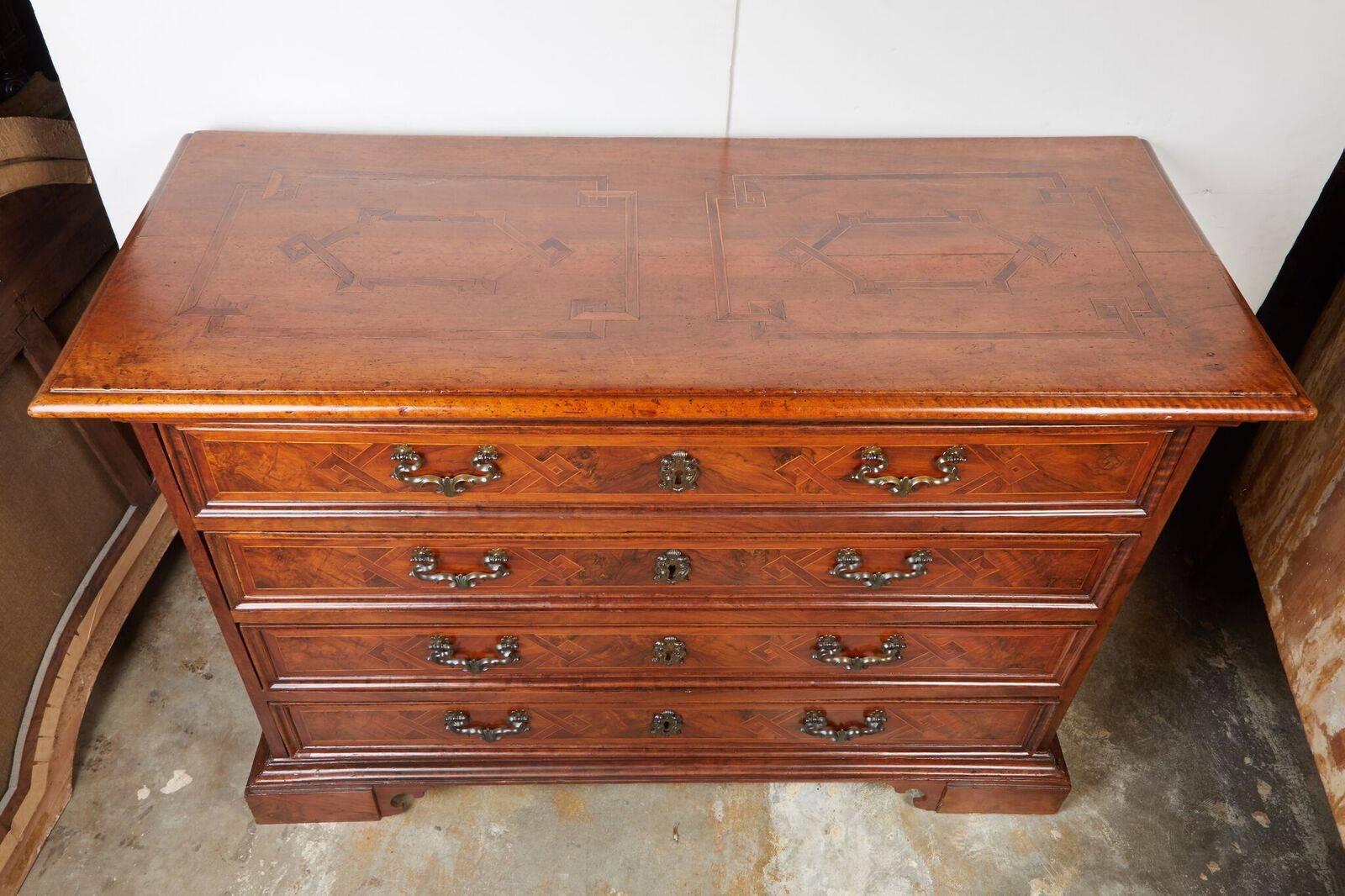 Handsome, Italian commode featuring four panelled drawers atop an elevated base. The piece is fully finished as the drawers, overhanging top and sides are inlaid with burl and pear woods with a repeating, geometric motif.