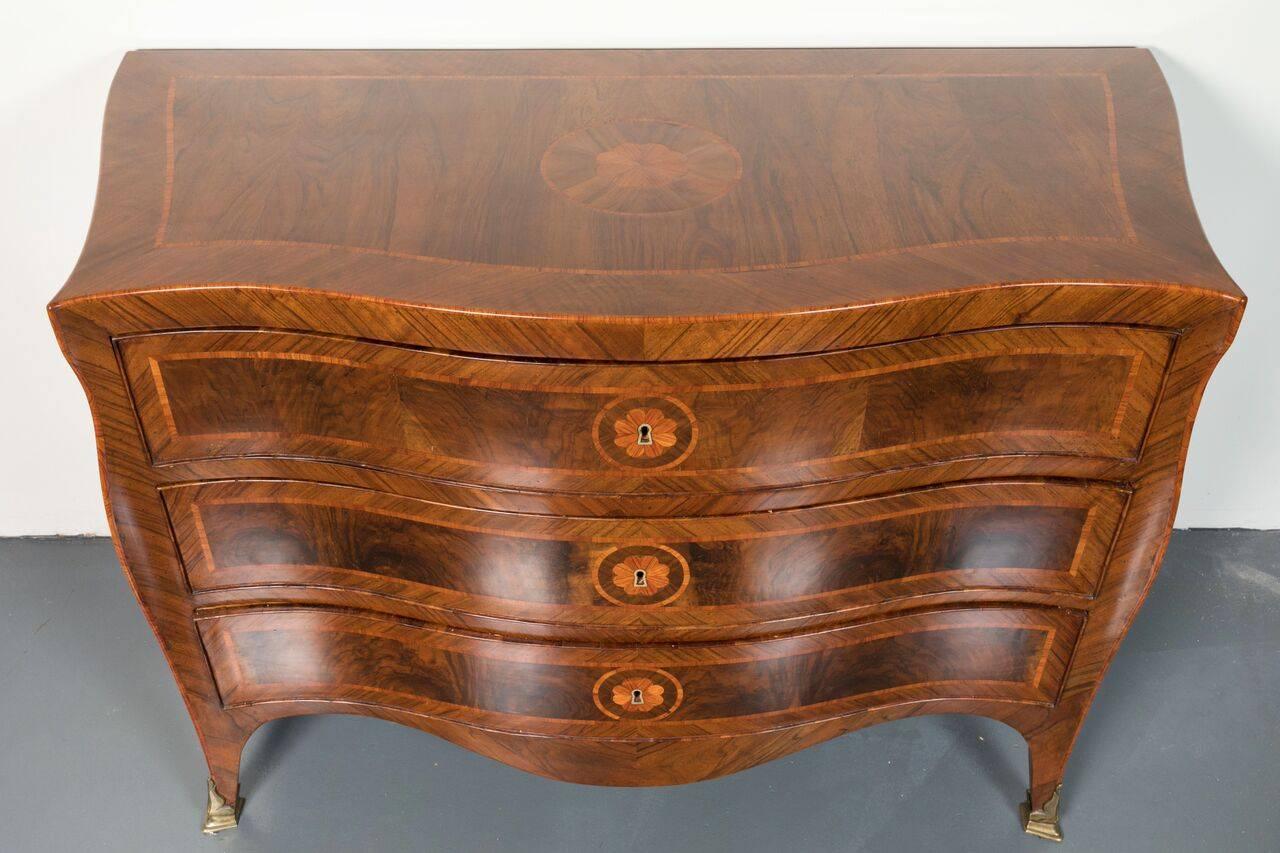 Elegant, three-drawer, serpentine, inlaid commode featuring a series of parquetry medallions. The whole atop ormolu capped feet.