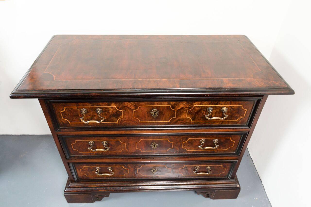 Hand-carved, ebonized walnut and burl, three-drawer commode with suites of contrasting, pearwood inlay on each drawer. The sides with raised panels. The whole on a stepped and bracketed base.