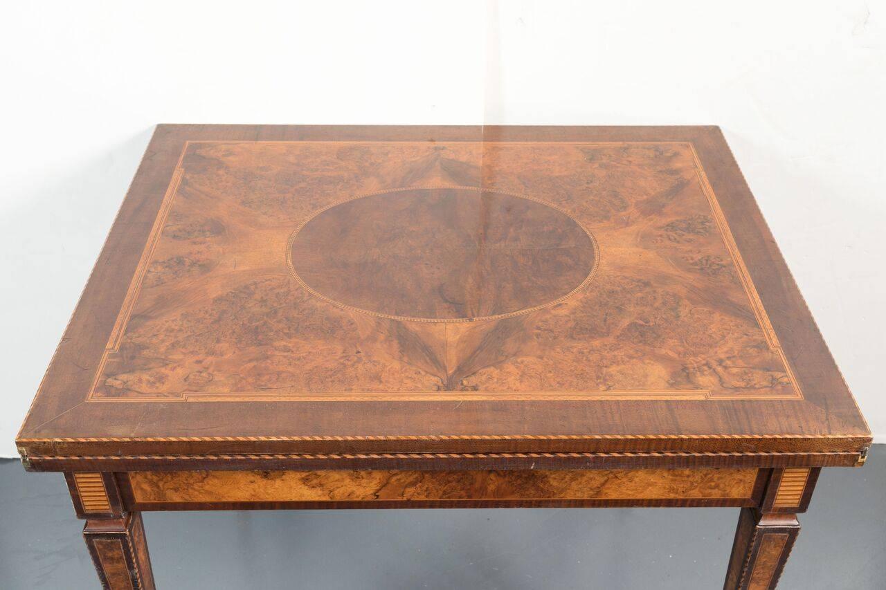 Empire style, flip-top games table richly veneered in burl, walnut and pear woods. The whole atop slender, tapered legs with ormolu feet.