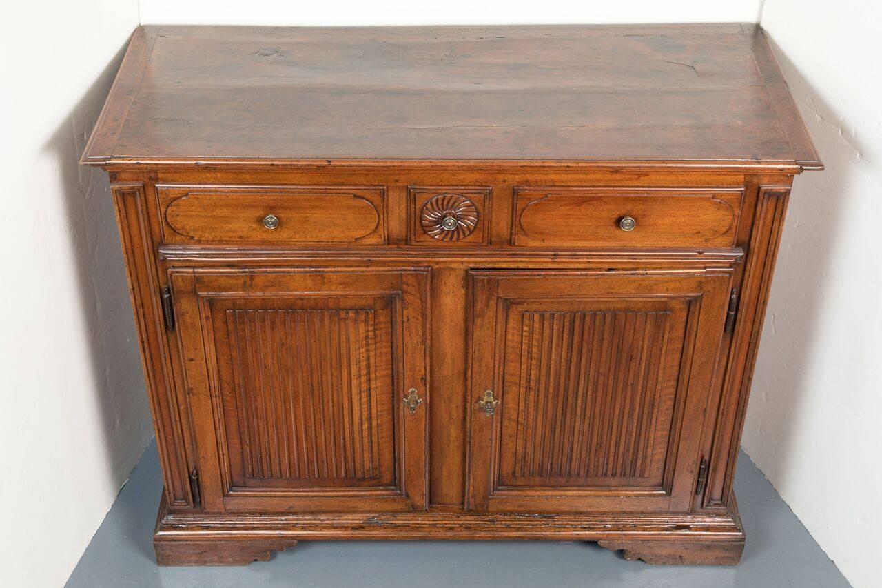 Hand-carved walnut cabinet with ribbed, panel doors below three-drawer of which the central one features a whirled. pinwheel relief. The whole on a raised bracket base. From the Piedmont region of Northern Italy.
