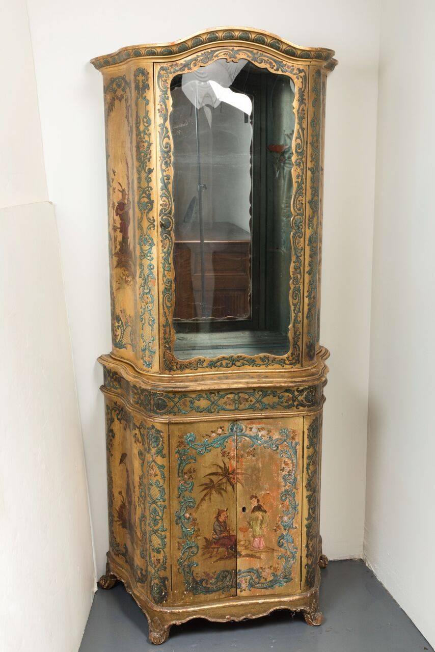 Beautifully hand-painted, slim, two-part, gilded, polychrome serpentine cabinet with a large, glass front display above two-door storage below.
