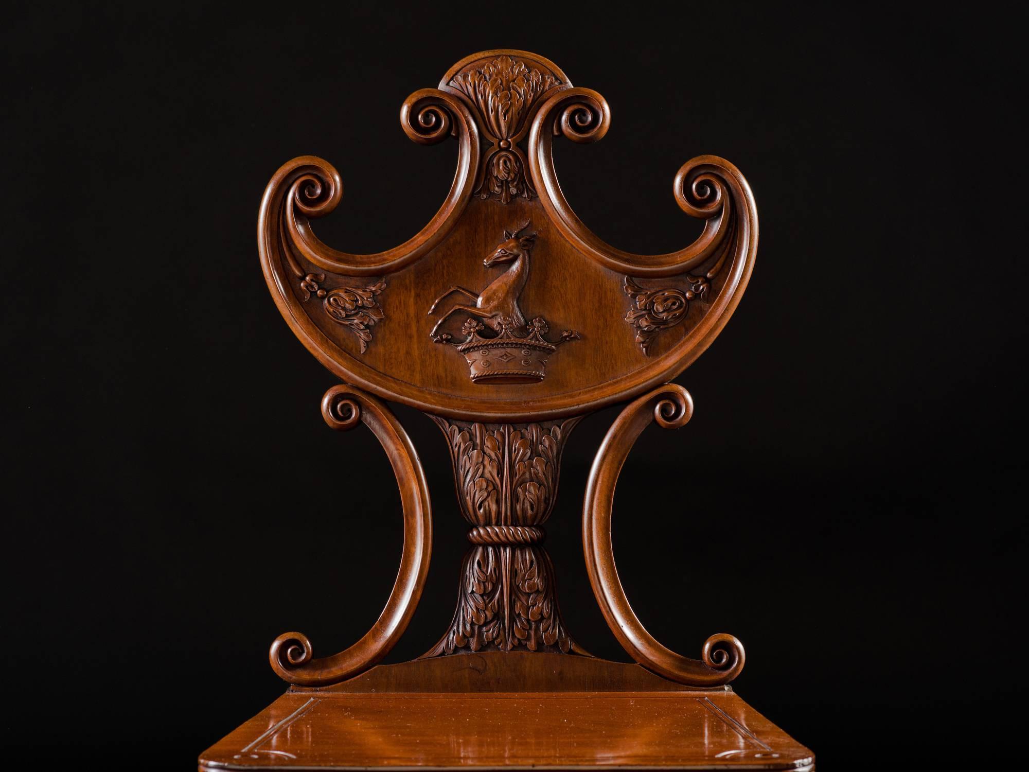 Each pelta-form backrest centred by a heraldic crest and supported on scroll-carved stiles centring a leaf-carved waisted support, each plank seat raised on turned, tapering reeded legs.

Sheraton in his cabinet dictionary (1803) introduces hall