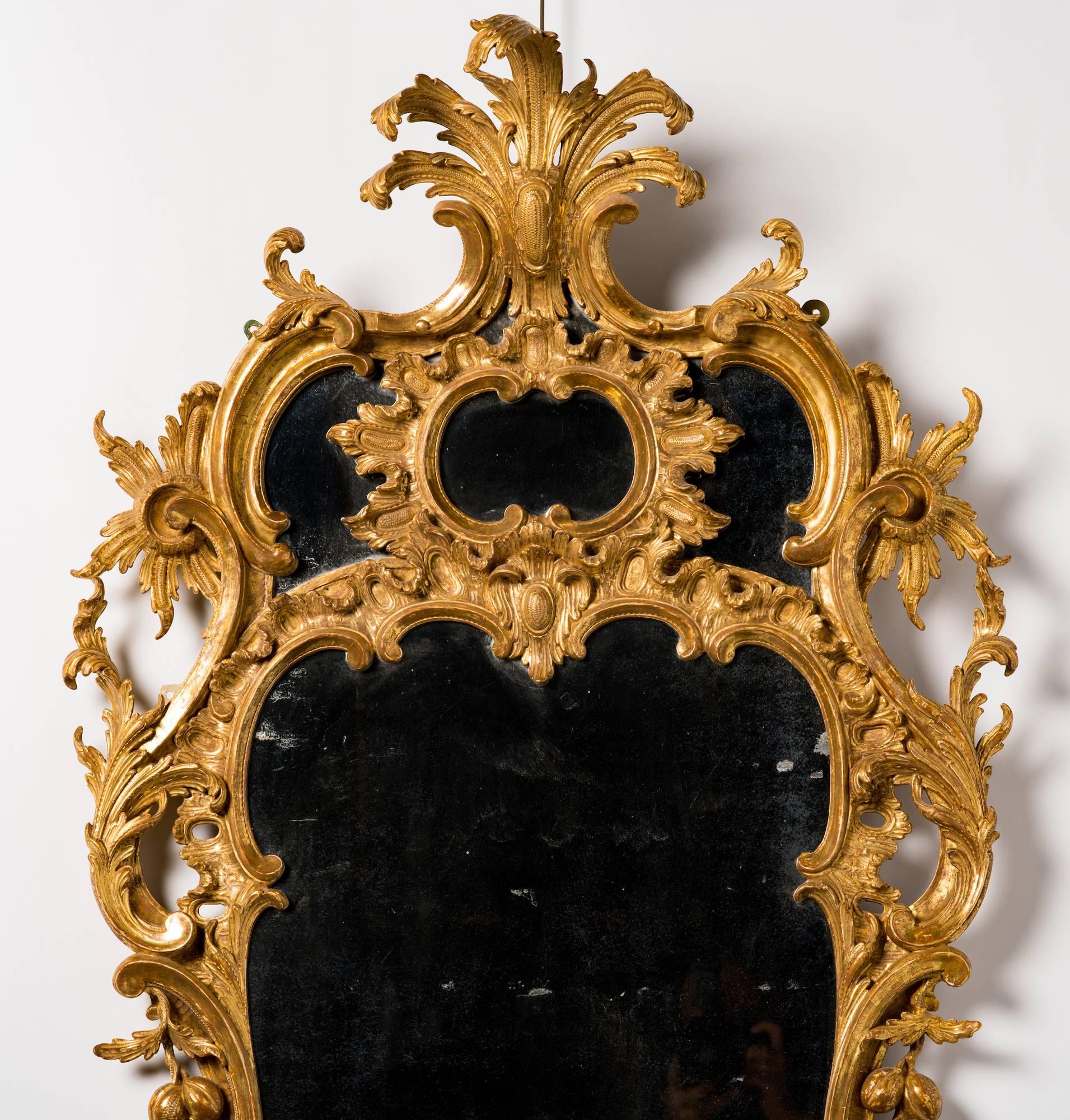 The pierced cartouche-shaped frame with leaf cresting above a divided mirror plate, carved with C-scrolls, cabochons, ruffles and fruiting vinery surrounding the central shaped mirror plate.