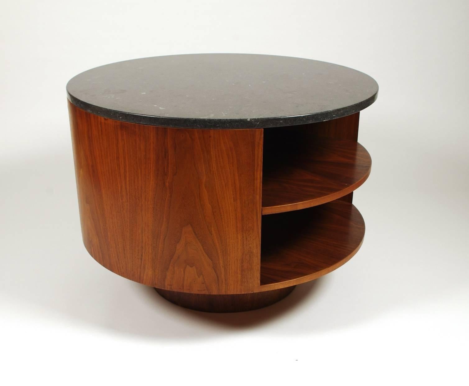 Vladimir Kagan walnut side table, the polished black marble top with numerous fossils; the round base with a single shelf raised on an inset plinth. Manufactured by Kagan-Dreyfus, New York.

Vladimir Kagan (1927-2016) enjoyed enormous popularity