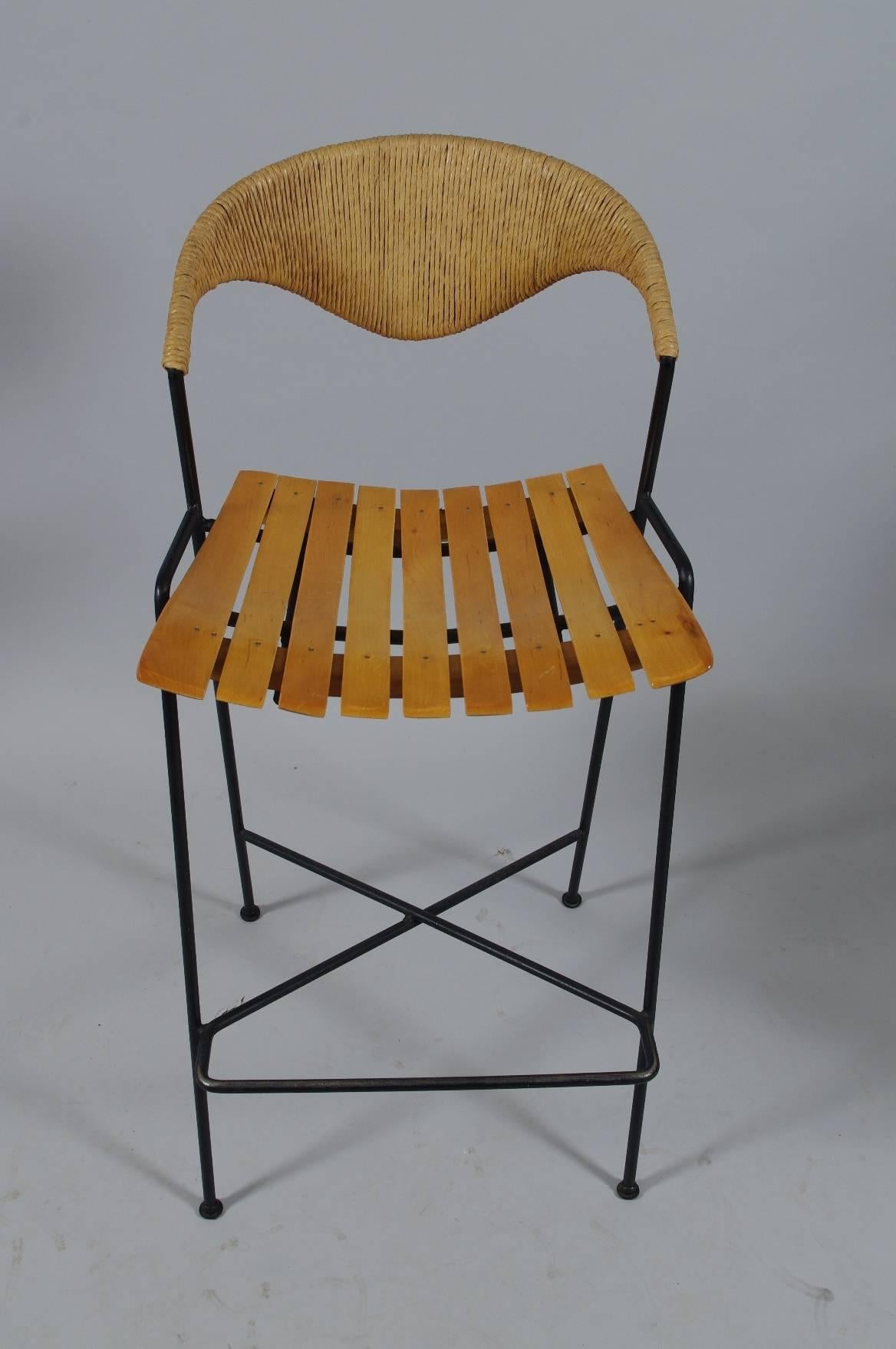 Set of three iron bar stools designed by Arthur Umanoff, each with a curved back wrapped in raffia over the slat seat (maple); the legs joined by a hairpin stretcher.

These comfortable chairs are in wonderful condition. They have never been