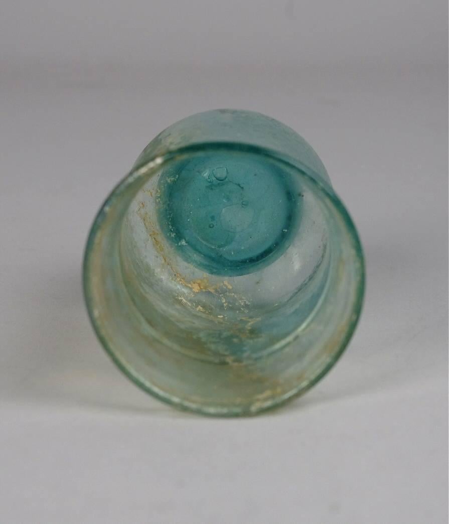 Ancient Roman glass beaker, blown in transparent pale blue glass; folded rim; thread applied around the upper body; solid base with pontil mark.

 For similar examples, see John W. Hayes, 