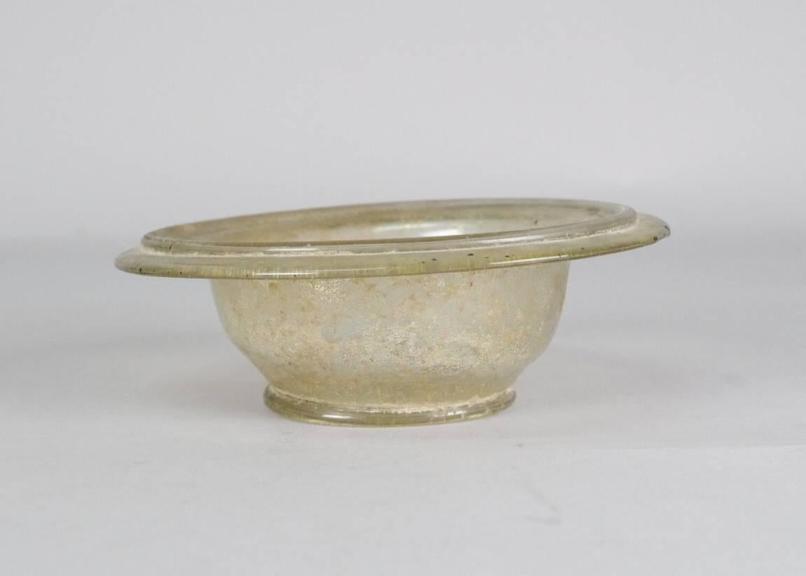 Ancient Roman glass bowl (patella cup), blown in clear glass; folded rim; small tubular pushed-in foot; floor kicked; pontil mark.

For a similar example, see John W. Hayes, 