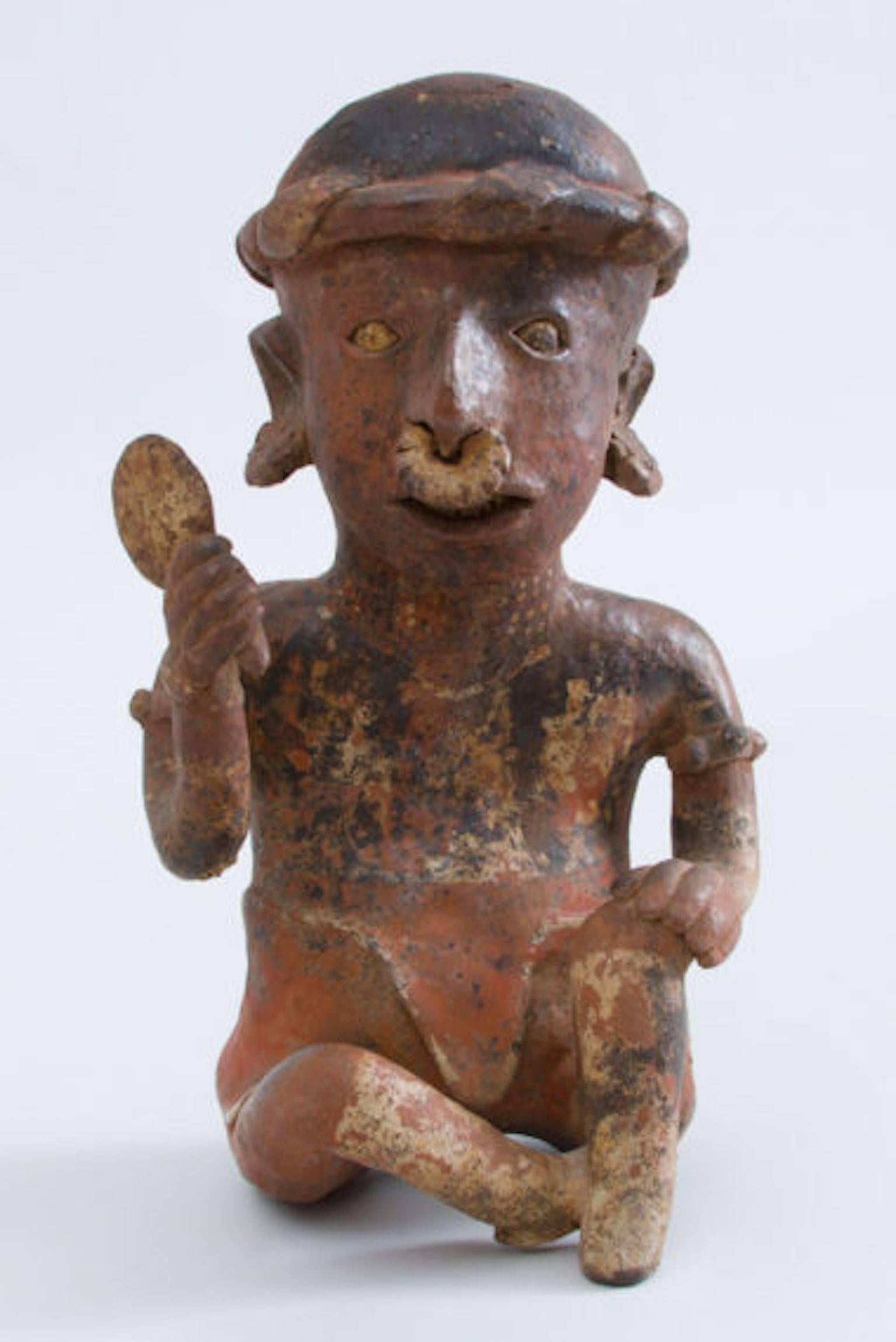 With left hand resting on the raised left knee, fan in the raised right hand, nose ring, ear ornaments, cap with band, and red, black and white pigment, signs of teeth in the mouth, Pre-Columbian (before 1492), Proto-Classical (50 BC – 250 AD), from