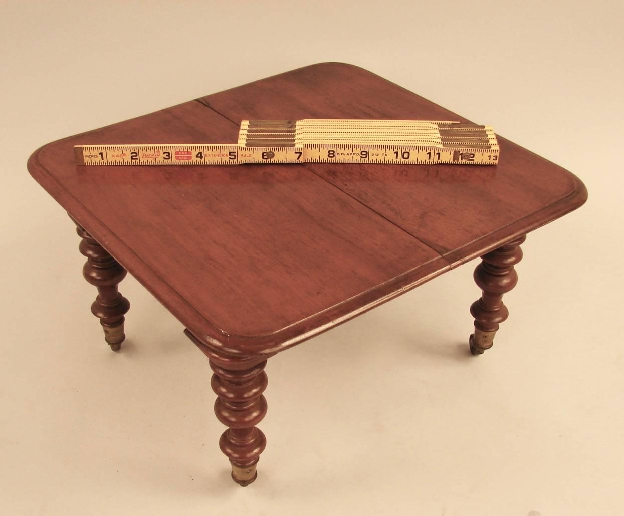 A well-crafted English Victorian salesman's sample of a mahogany 3-leaf dining table, complete with leaf holder, the table with turned legs ending in brass casters. Possibly a piece of doll house furniture.