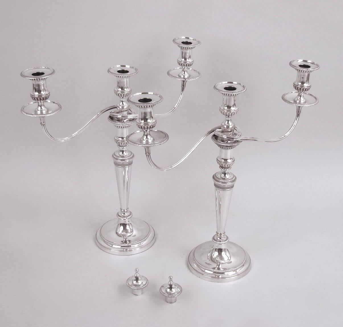A nice pair of English columnar convertible three-branch candelabra in the neoclassical taste, the removable arms with finials (useable with two or three lights or as candlesticks) each urn form nozzle with beaded rims and conforming bases, circa