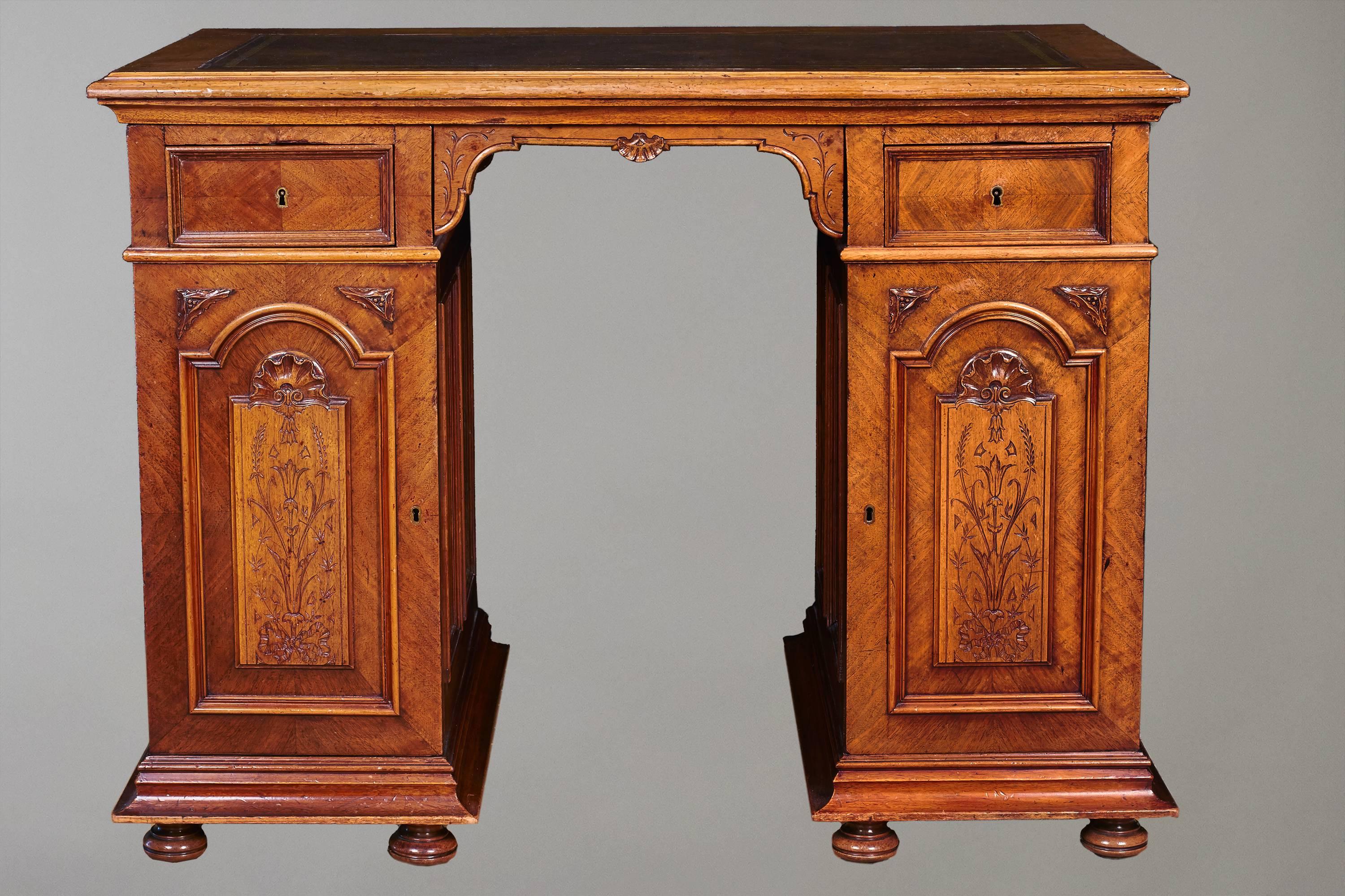 An unusual compact English walnut pedestal desk, the leather-lined top above two frieze drawers over two shell carved and incised paneled doors, the sides and back paneled as well, supported on compressed bun feet.