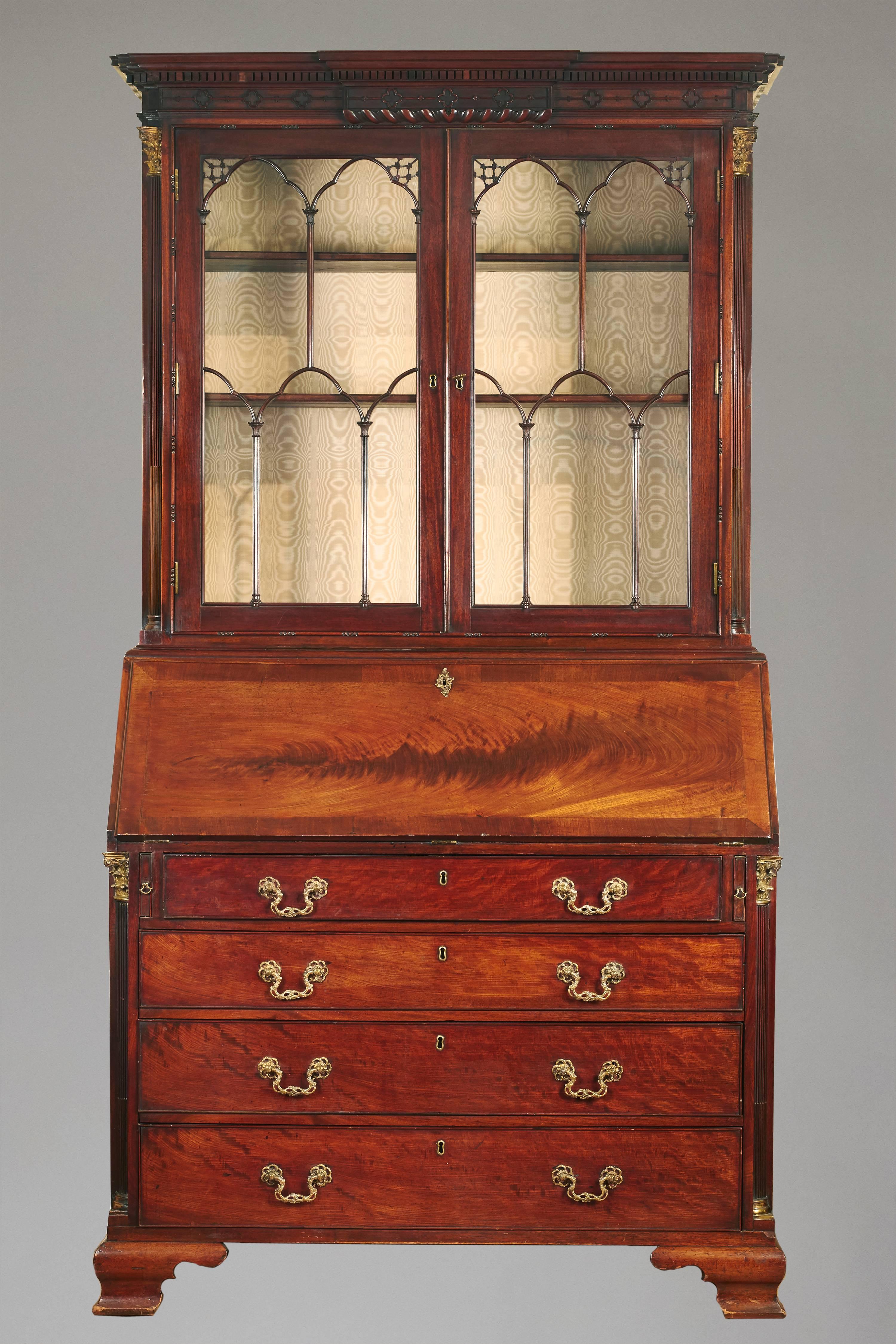 A fine quality George III period brass-mounted figured mahogany bureau bookcase, the elaborately carved pediment above two glazed doors flanked by stop fluted columns with brass capitals, the central fall front desk with a well-fitted interior,