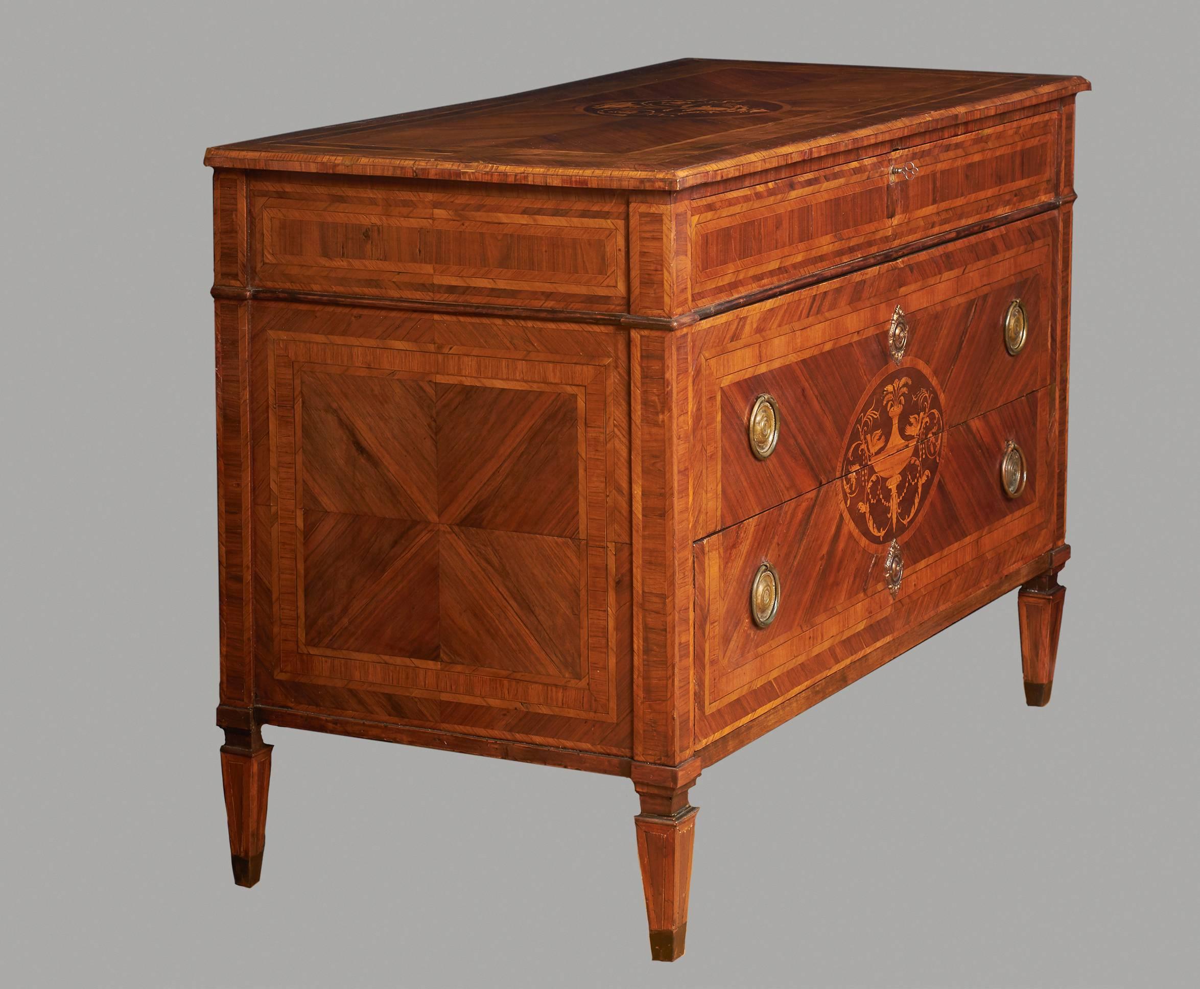 An Italian neoclassical inlaid walnut commode with one shallow and two deep drawers, the top with central foliate tulipwood, rosewood and kingwood inlay, the drawers with stylized urn inlay, circa 1790. Drawers now lined with old silk.