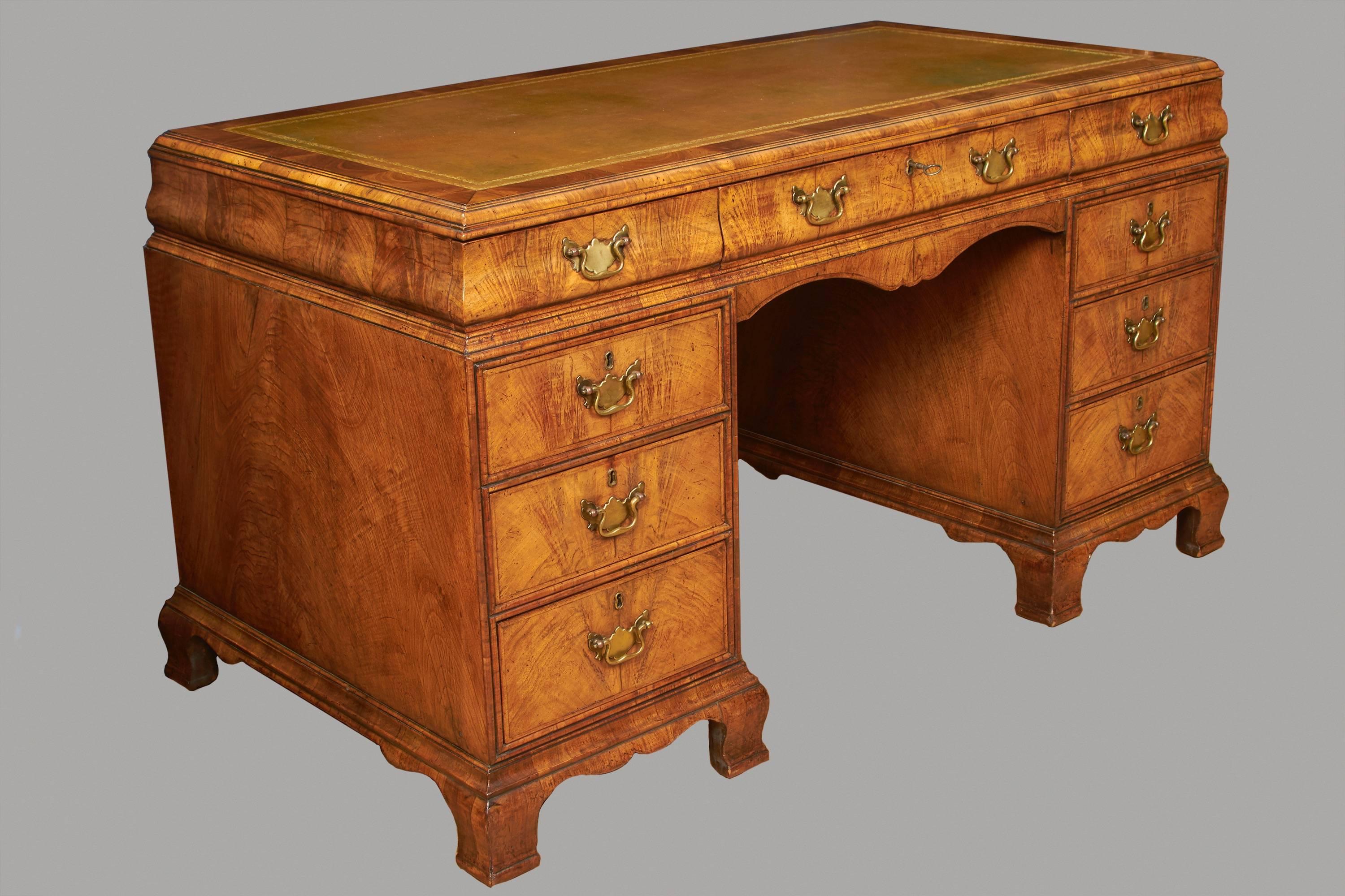 An English burl walnut pedestal desk of attractive size with a gilt-tooled leather top over three bombe frieze drawers and kneehole apron above flanking sets of three short drawers with a paneled back, all supported on ogee bracket feet, early 20th