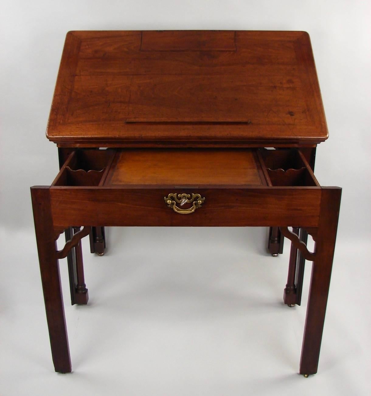 A George II period mahogany drafting or architect's table, the adjustable top with a built-in bookrest and a separate adjustable candle support, the pull-out interior with a retractable brown tooled leather surface flanked by wells, all supported on