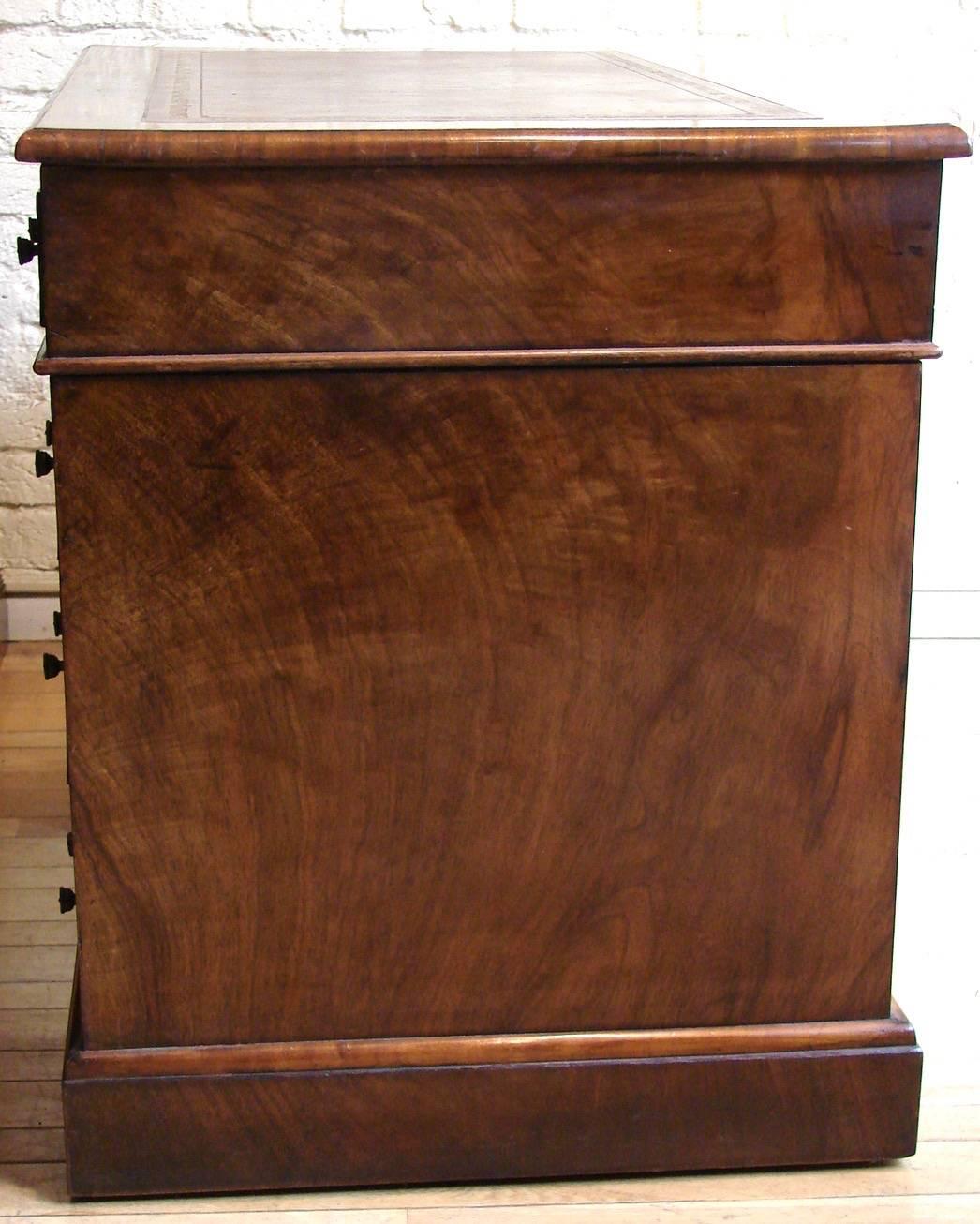 A pretty English Georgian style burl walnut pedestal desk, the gilt-tooled brown leather lined top above three frieze drawers over two pedestals, each with three graduated short drawers, all resting on a plinth base with concealed casters, circa