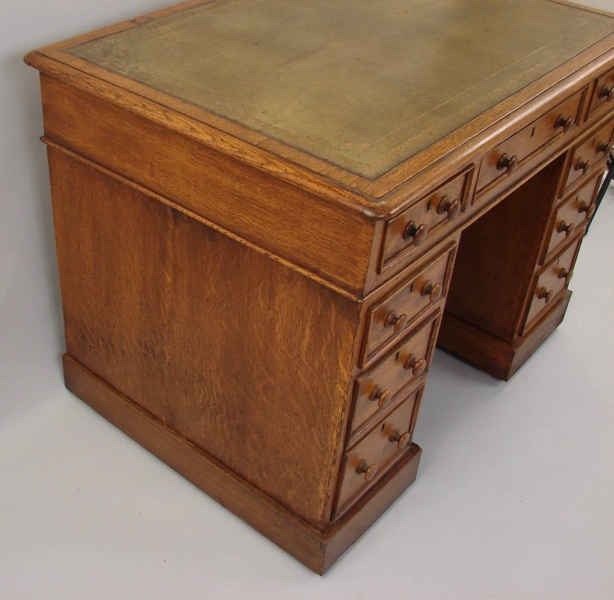 A charming small English oak pedestal desk, the khaki colored gilt-tooled leather top over three frieze drawers above two pedestals, each with three graduated short drawers, all on a plinth base, circa 1880. Possibly a child's desk.