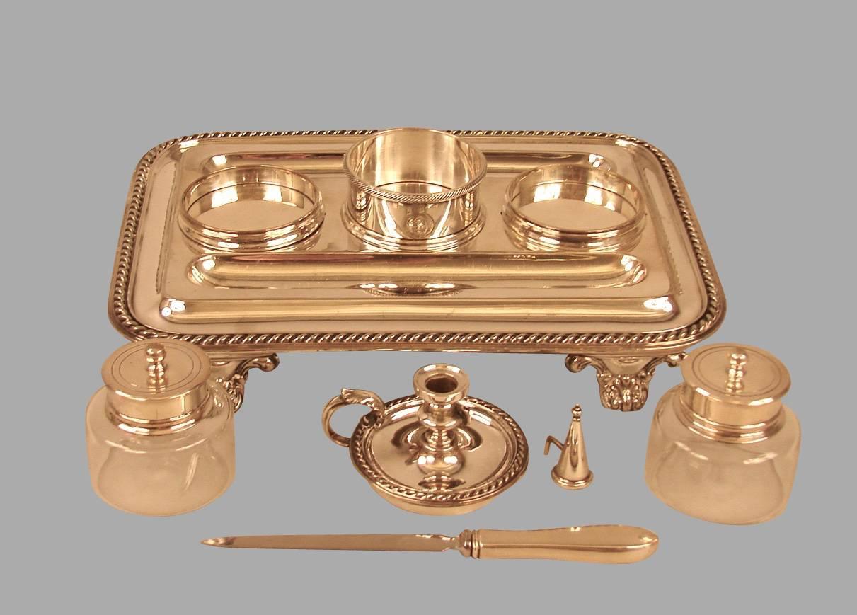An English silver plate ink stand with double pen reservoirs fitted with a pair of covered ink jars flanking the chamber stick mounted with a snuffer, resting on figural supports below a gadrooned edge, circa 1850. 