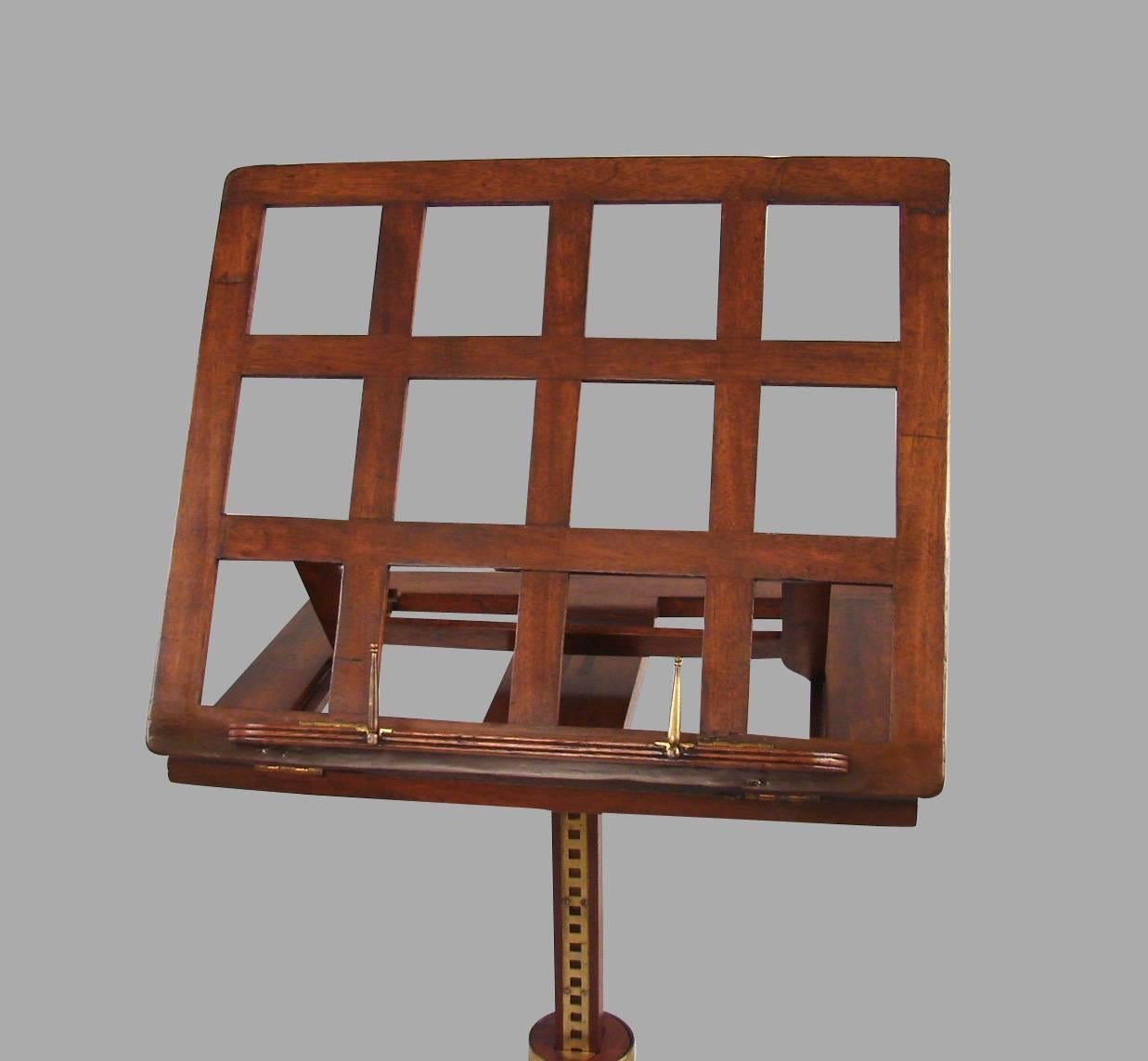 A Regency mahogany music stand, the top with a ratcheted mechanism supported on an adjustable square column with an embossed brass band, terminating in a turned column supported by a molded tripod base ending in brass box casters, circa 1800-1820.