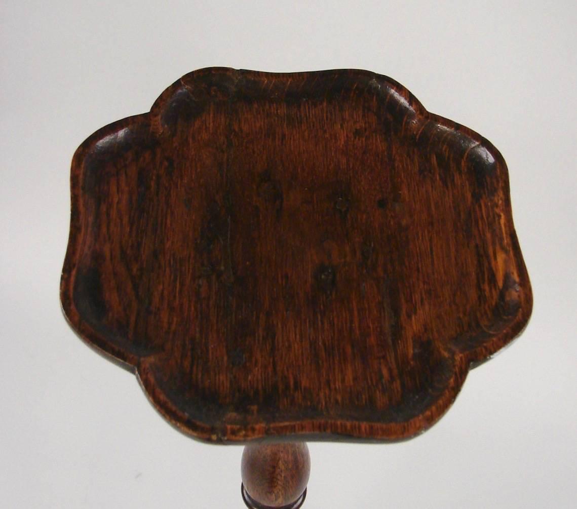 A provincial George III oak torchere, the pie crust top supported on a ring turned standard terminating in a tripod base with pad feet, circa 1770.
