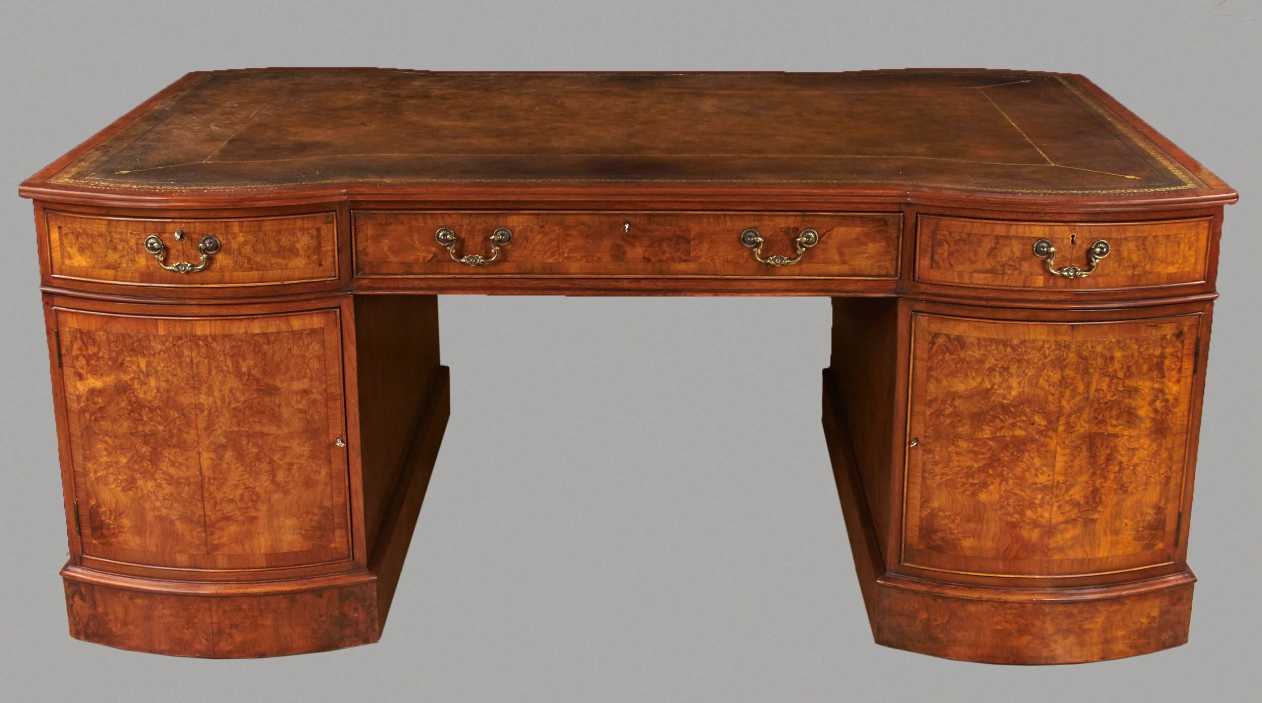 A good quality English Georgian style figured walnut partner's desk, the gilt-tooled brown leather top with a moulded edge above two banks of convex graduated pedestal drawers, the back with frieze drawers above cabinet doors each enclosing a single