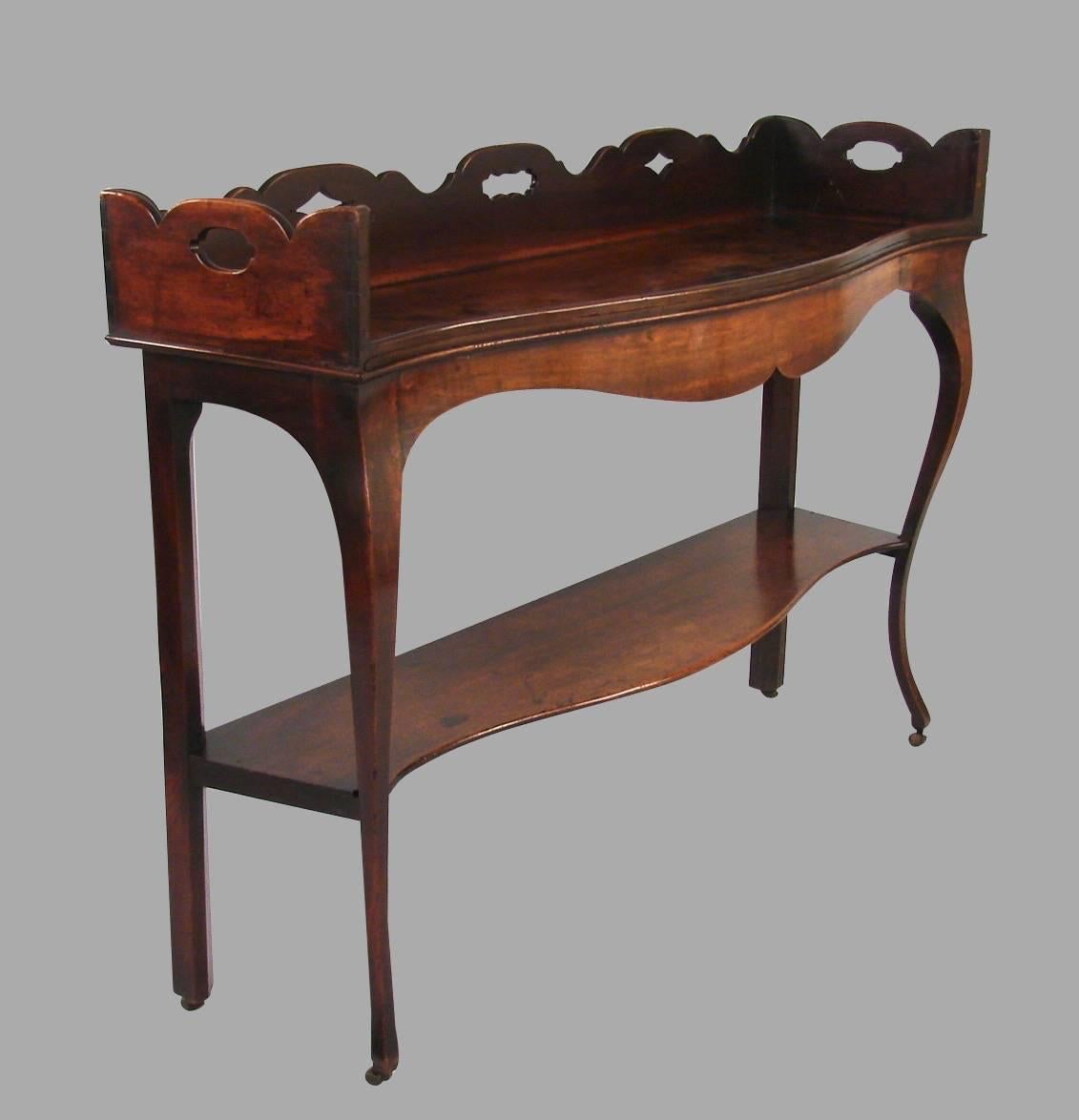 An unusual George III period server in the Hepplewhite taste, the serpentine top with a pierced surround above a molded edge with a shaped apron above a single shelf supported on front cabriole legs ending in original casters, circa 1790.