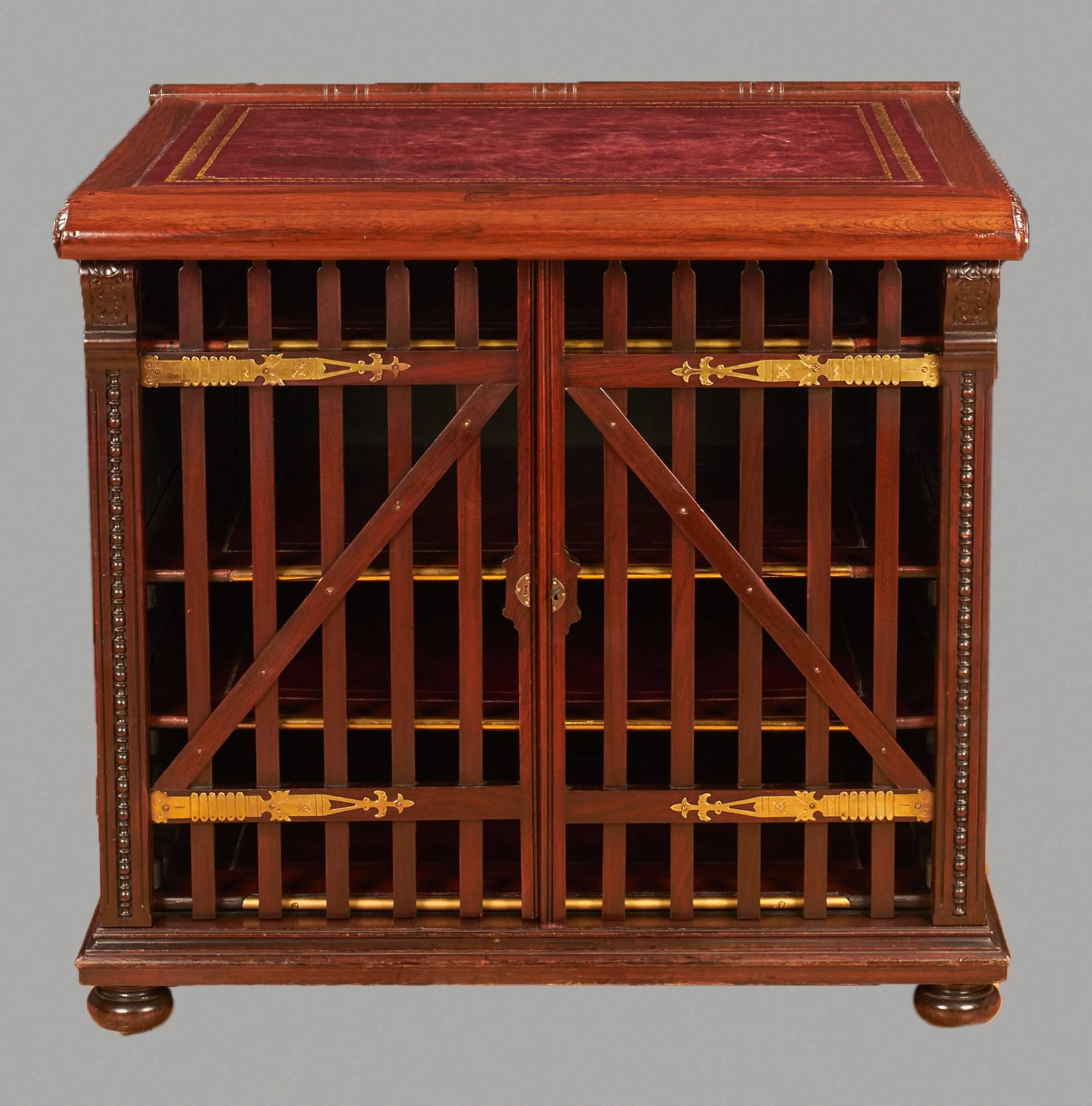 An unusual English rosewood library folio cabinet, the burgundy gilt-tooled inset leather lined top opening to a well, above four leather lined shelves enclosed by a pair of brass-mounted gate form doors, the sides and back with figured panels