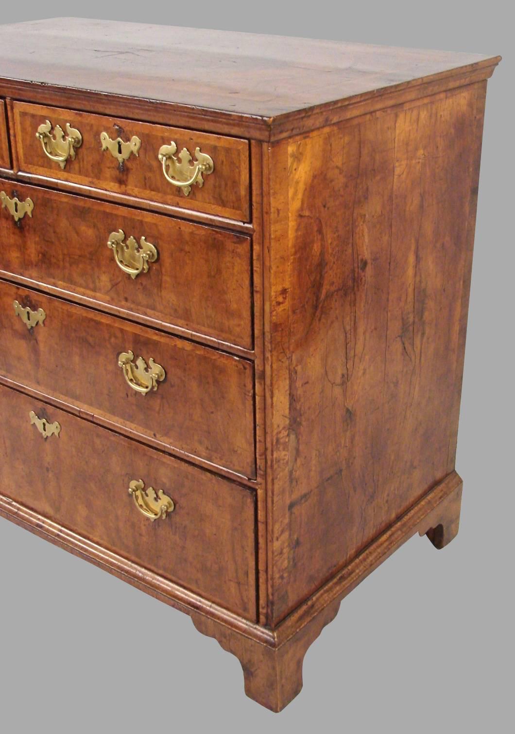 A fine quality George I period inlaid walnut five-drawer chest, the feather-banded top with a beautifully figured walnut inlaid oval central panel over two short and three long drawers, all feather-banded, resting on bracket feet. Both sides