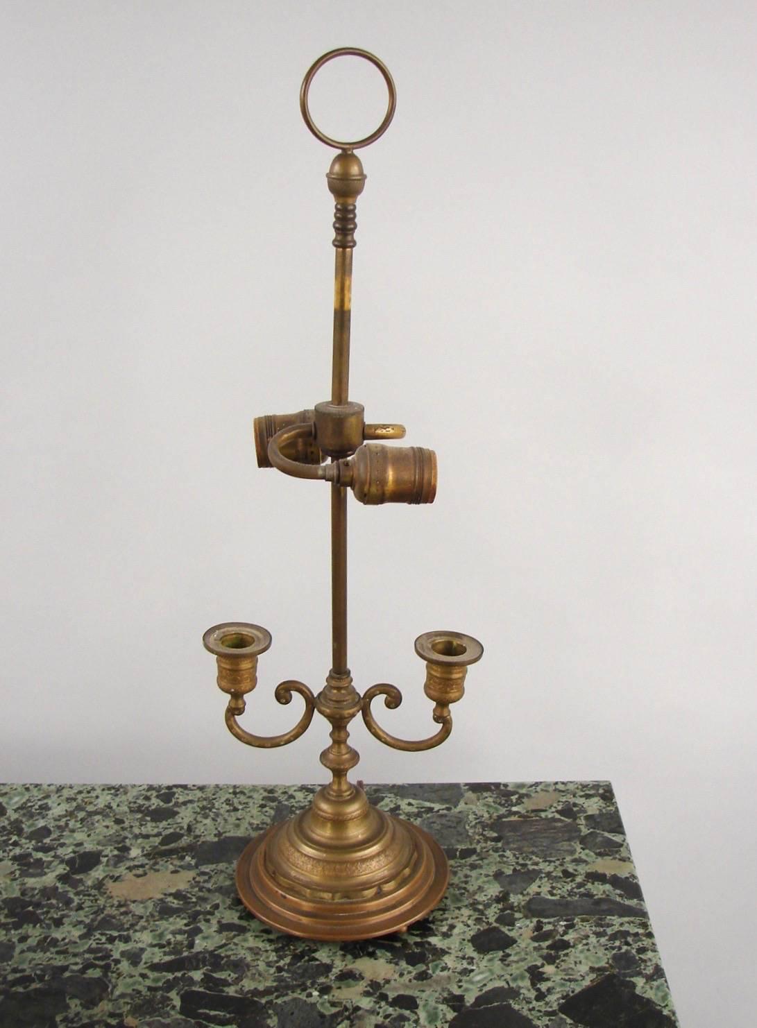 A French brass two-light bouillotte lamp, the metal shade decorated with gilt mermaids and concealing an electrical fitting above two brass candle arms supported on a circular tiered base.