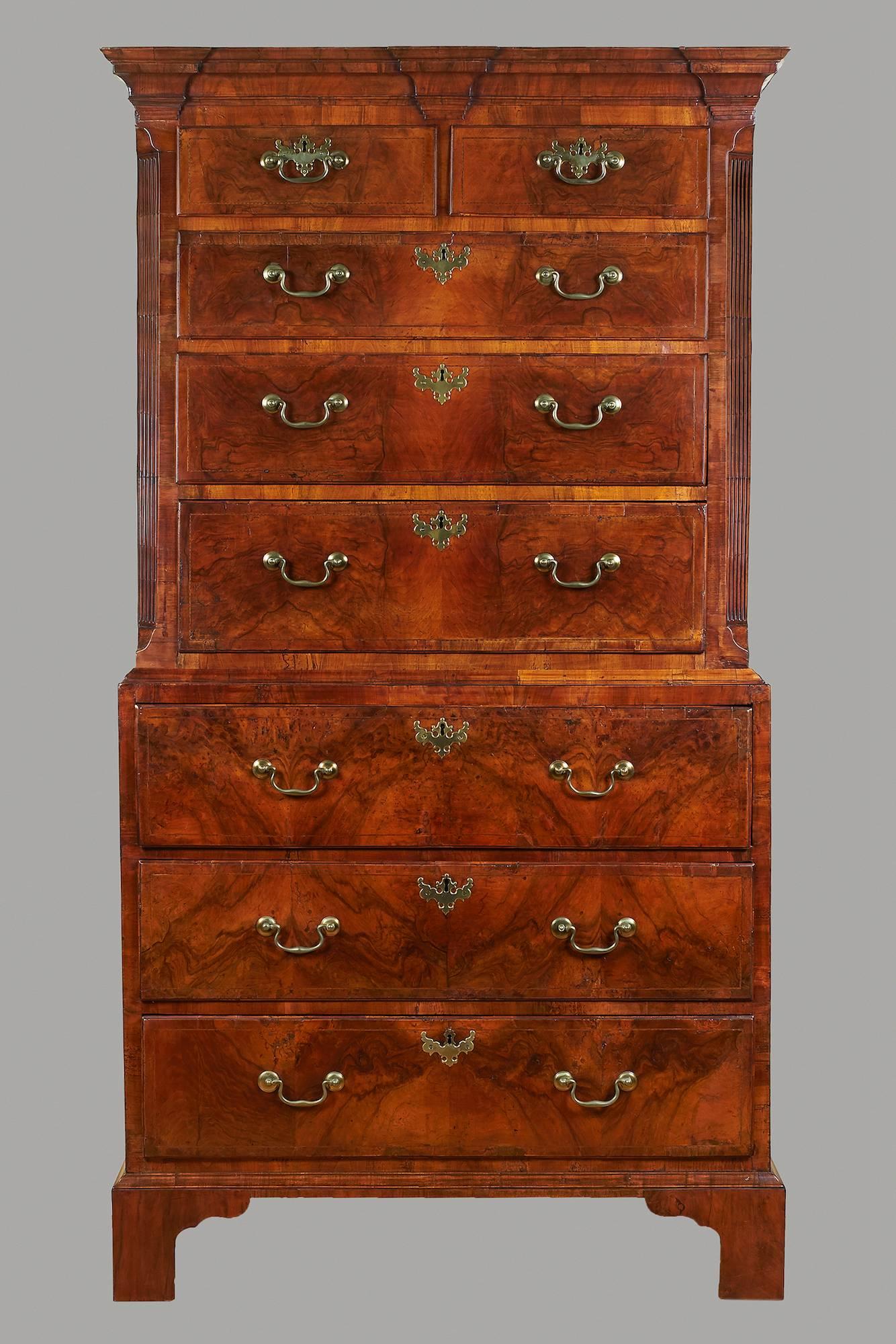 A George II walnut chest-on-chest in two parts, the cornice decorated with three capitals over two short and three long line inlaid drawers framed by fluted quarter columns, the lower stage containing a well-fitted amphitheater style secretaire