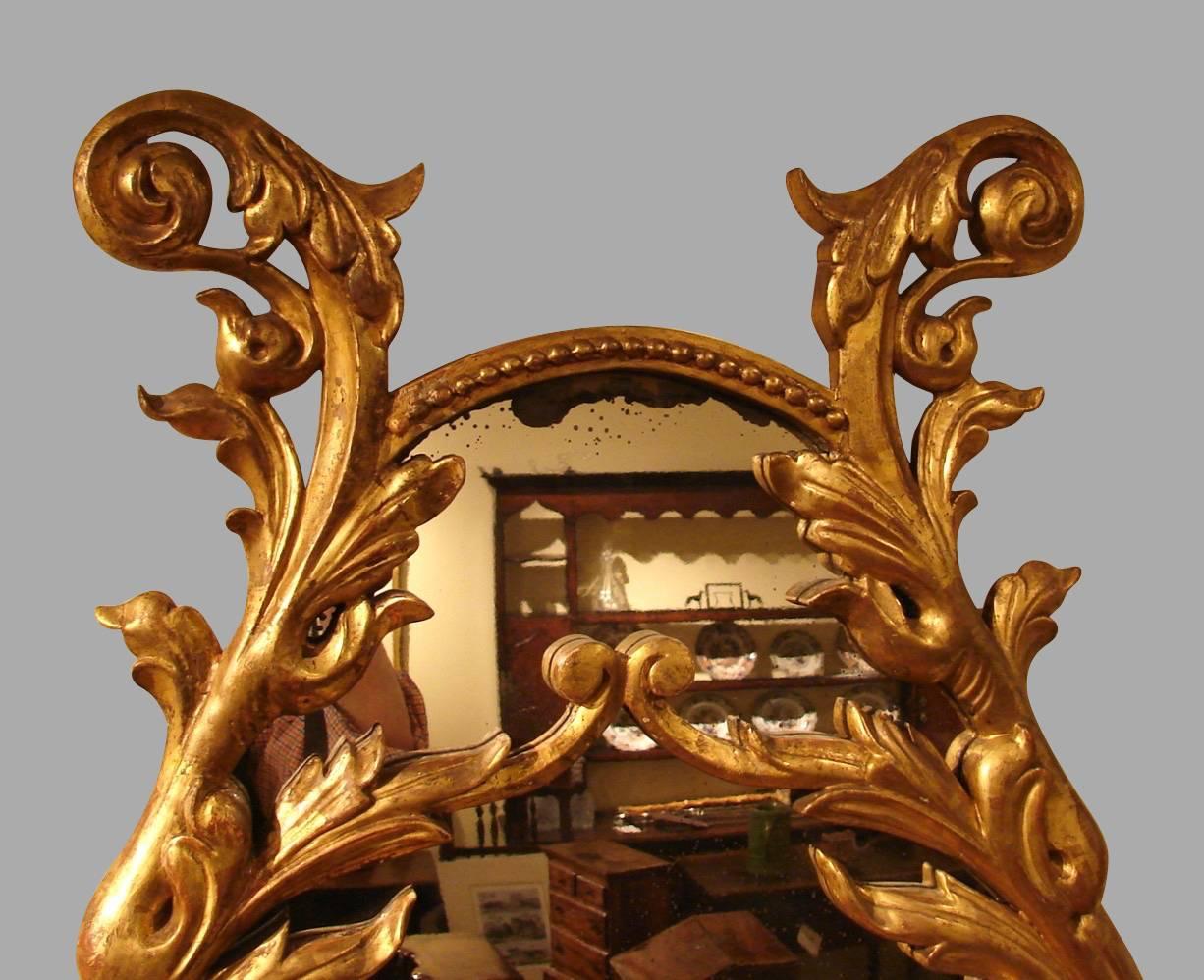 A pretty lyre shaped neoclassical Italian giltwood mirror retaining its original glass, the plate framed by foliate scrolls centered by a beaded circle above an embossed molded plinth base, circa 1825.