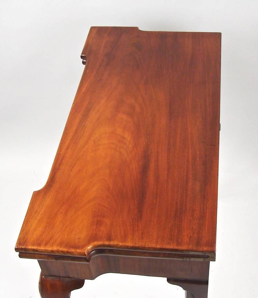 A George II mahogany or red walnut games table, the flip-top fitted with corner candle insets and 4 guinea wells, lined in felt and supported by a single rear swing leg, above a single drawer, resting on front cabriole legs with ball and claw feet,