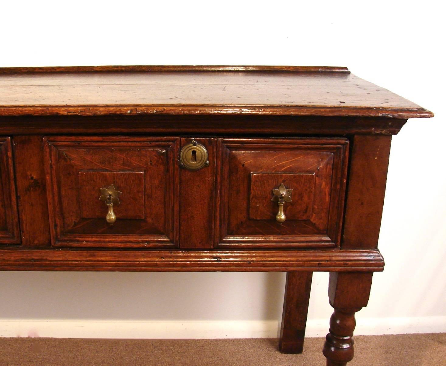 An English oak dresser base, the top with a moulded edge above three fitted panel front drawers raised on turned front and stile rear legs, circa 1680 and later.
Raised in height, two drawers relined.