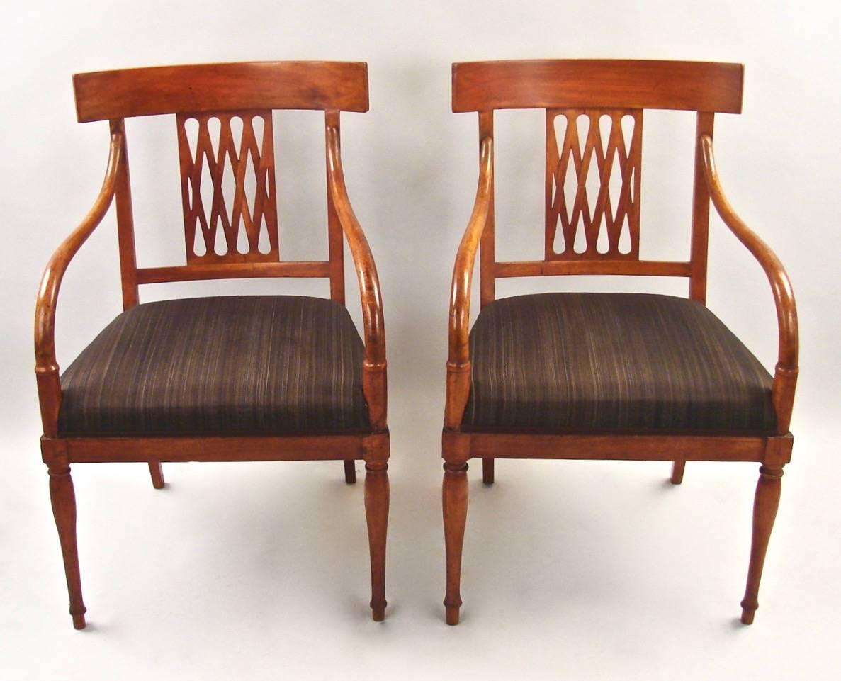 An attractive pair of fruitwood or pale mahogany open armchairs in the neoclassical taste, the rectangular crest rail above a geometric splat, the down swept arms terminating in the seat rail supported on tapered turned legs, circa 1820.