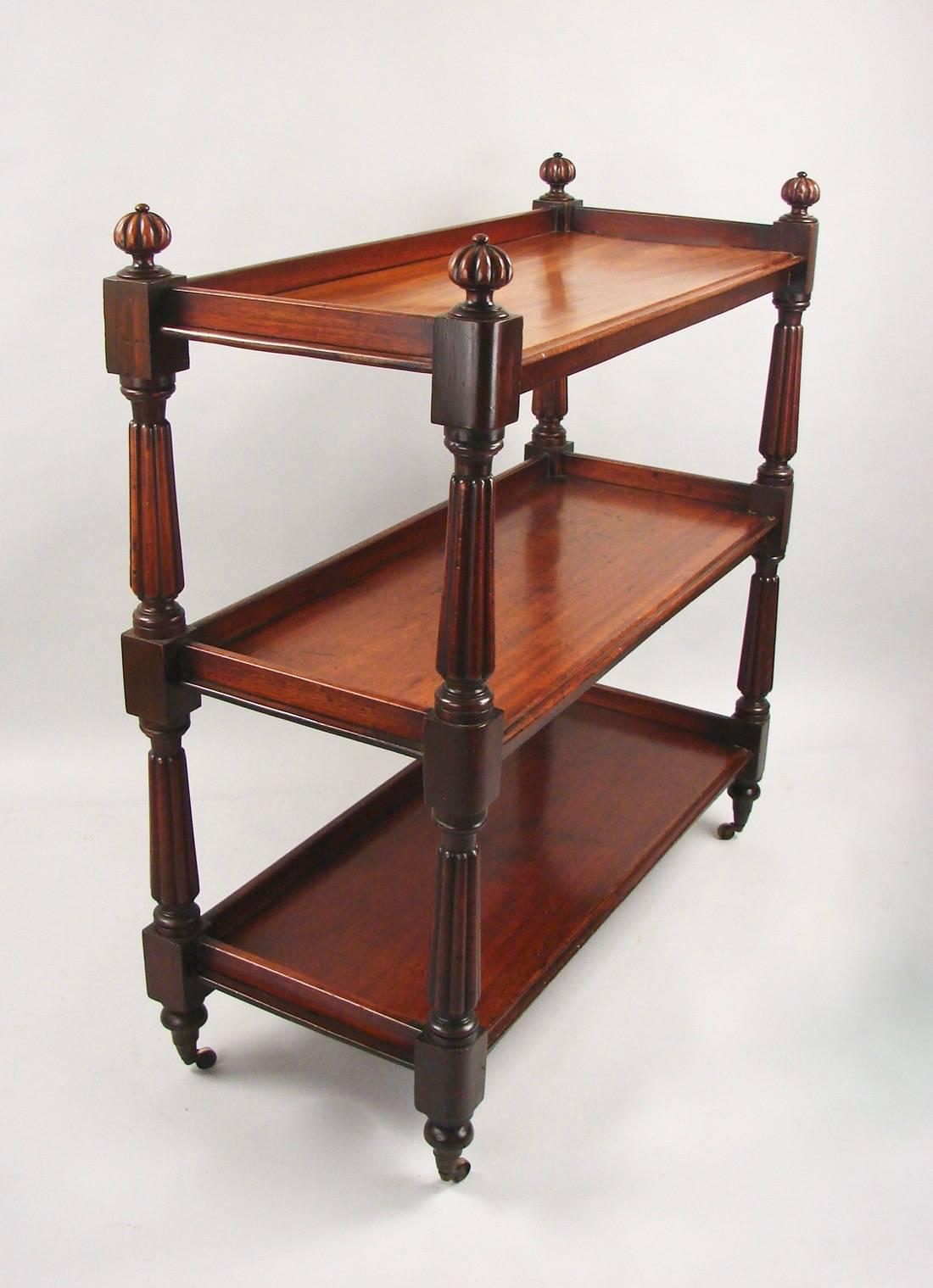 An English mahogany three-tier server, each shelf with a molded edge, supported by fluted columns headed by carved finials, all resting on turned feet ending in casters, circa 1870.