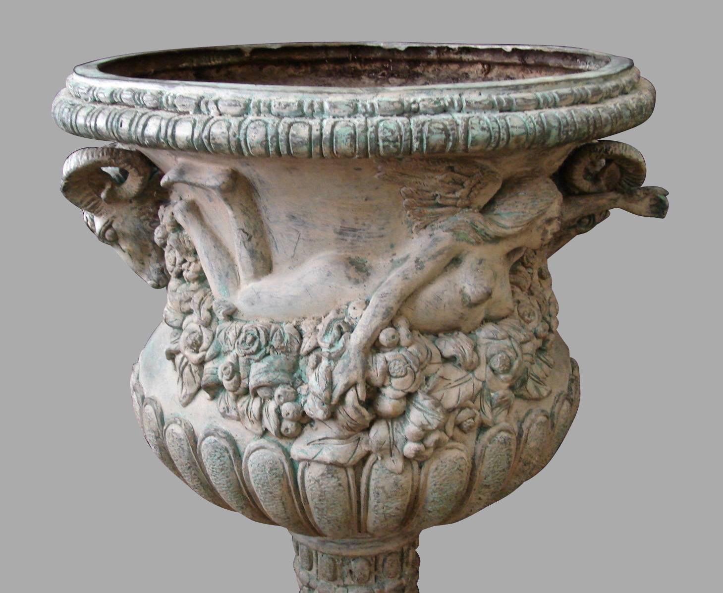 An impressive pair of neoclassical style bronze planters, the handles in the form of ram's heads the vases further decorated with female nudes and garlands of flowers and leaves above a stand with classical motifs encircled with acanthus leaves on