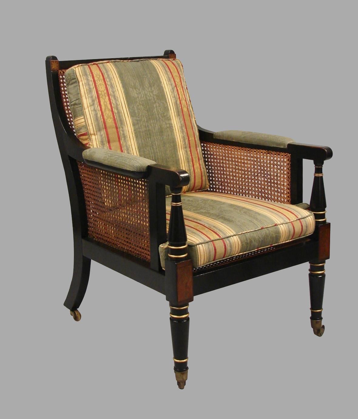 A fine pair of Regency painted and caned beechwood arm chairs, the crest rail inlaid at the corners with rosewood and brass stars, the padded arms above gold accented ring turnings, the seat rail embellished with brass and rosewood inlaid blocks at