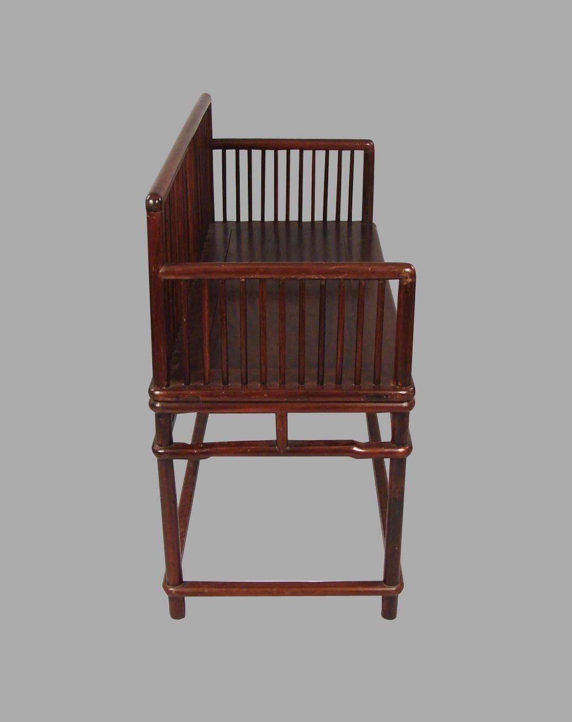 A Chinese Ming style hardwood spindle back bench with a paneled seat and spindled sides, supported on an elegant Ming style base, 19th century.