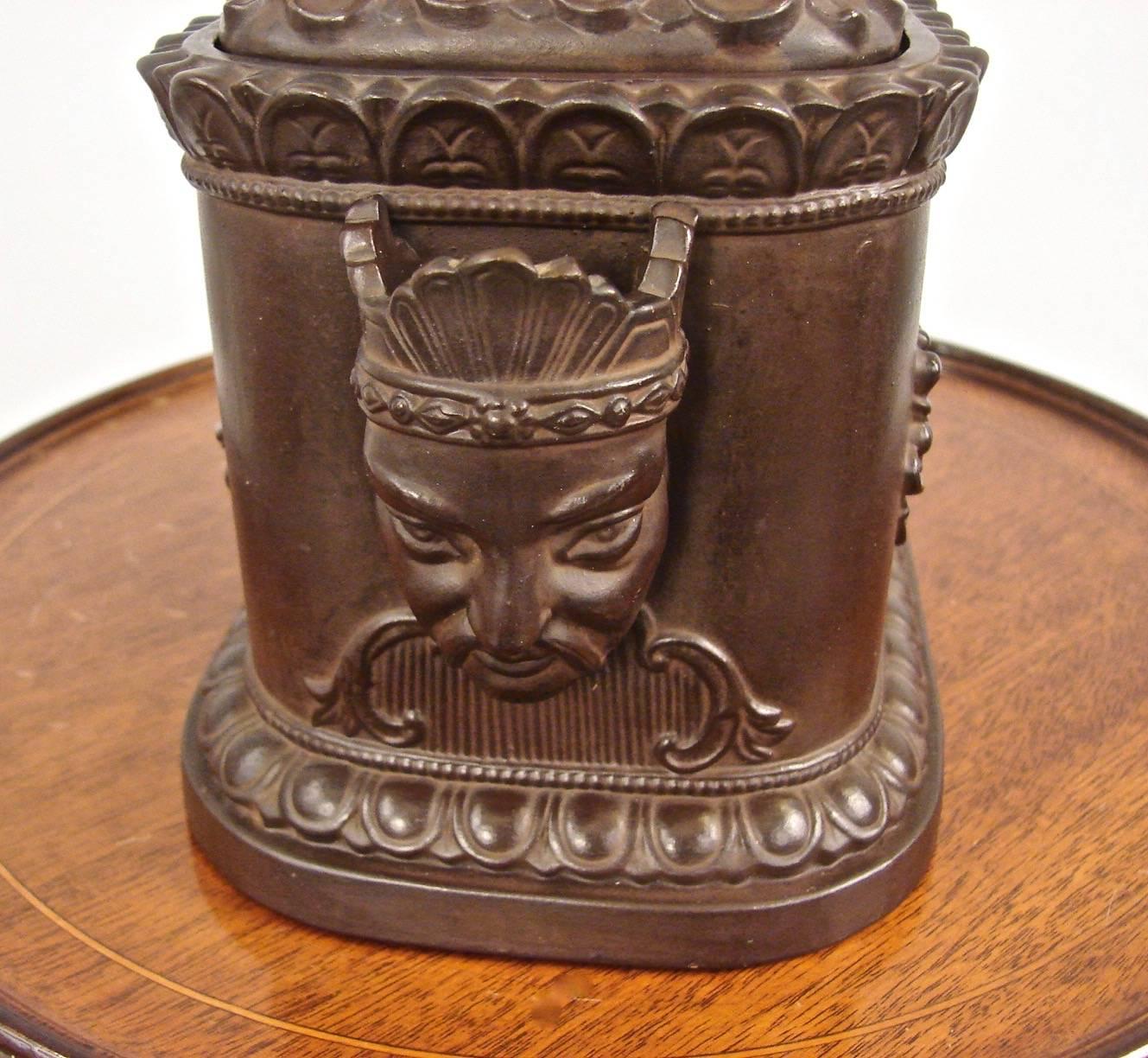 A very decorative late Regency period chocolate brown earthenware humidor, the top with a well-modeled whippet finial, the sides decorated with stylized Chinese faces, the long sides decorated with smoking accoutrements possibly opium pipes, resting