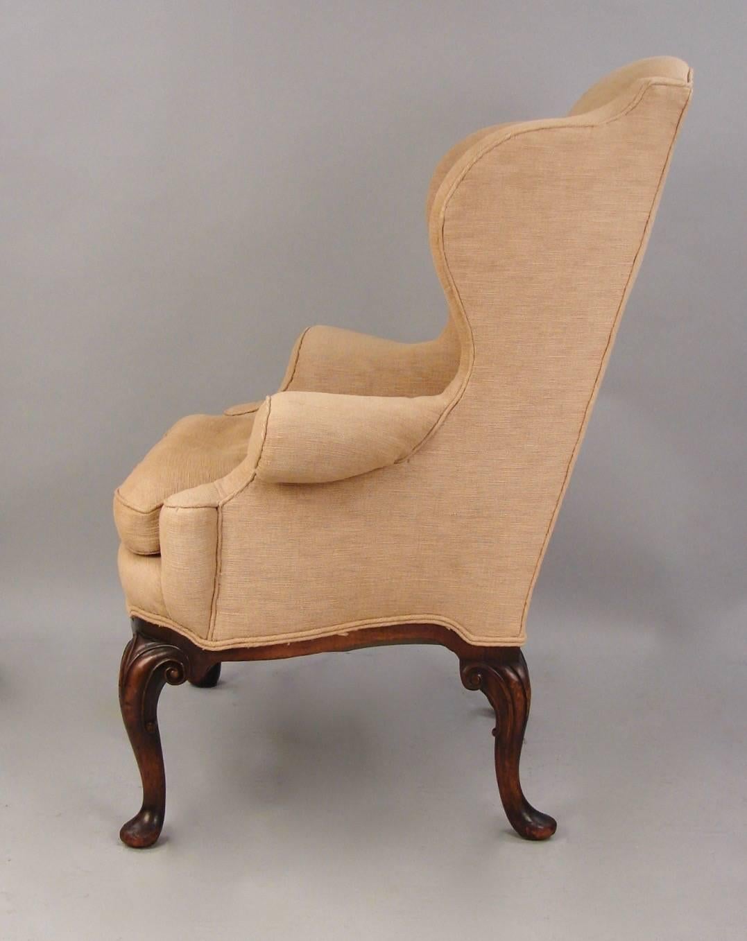 An attractive and comfortable George II style wingback armchair upholstered in a cream colored silk-linen ribbed fabric resting on carved mahogany cabriole legs ending in pad feet, circa 1900.
 