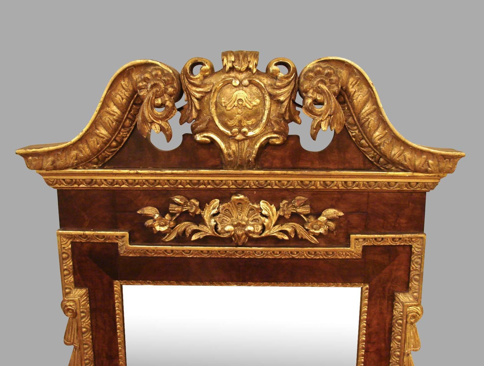 A George III walnut parcel-gilt wall mirror, the gilded swan neck pediments each terminating in a flower rosette with trailing leaves above a gadrooned edge over a carved and gilt central foliate decoration, the mirror framed by an inner border of